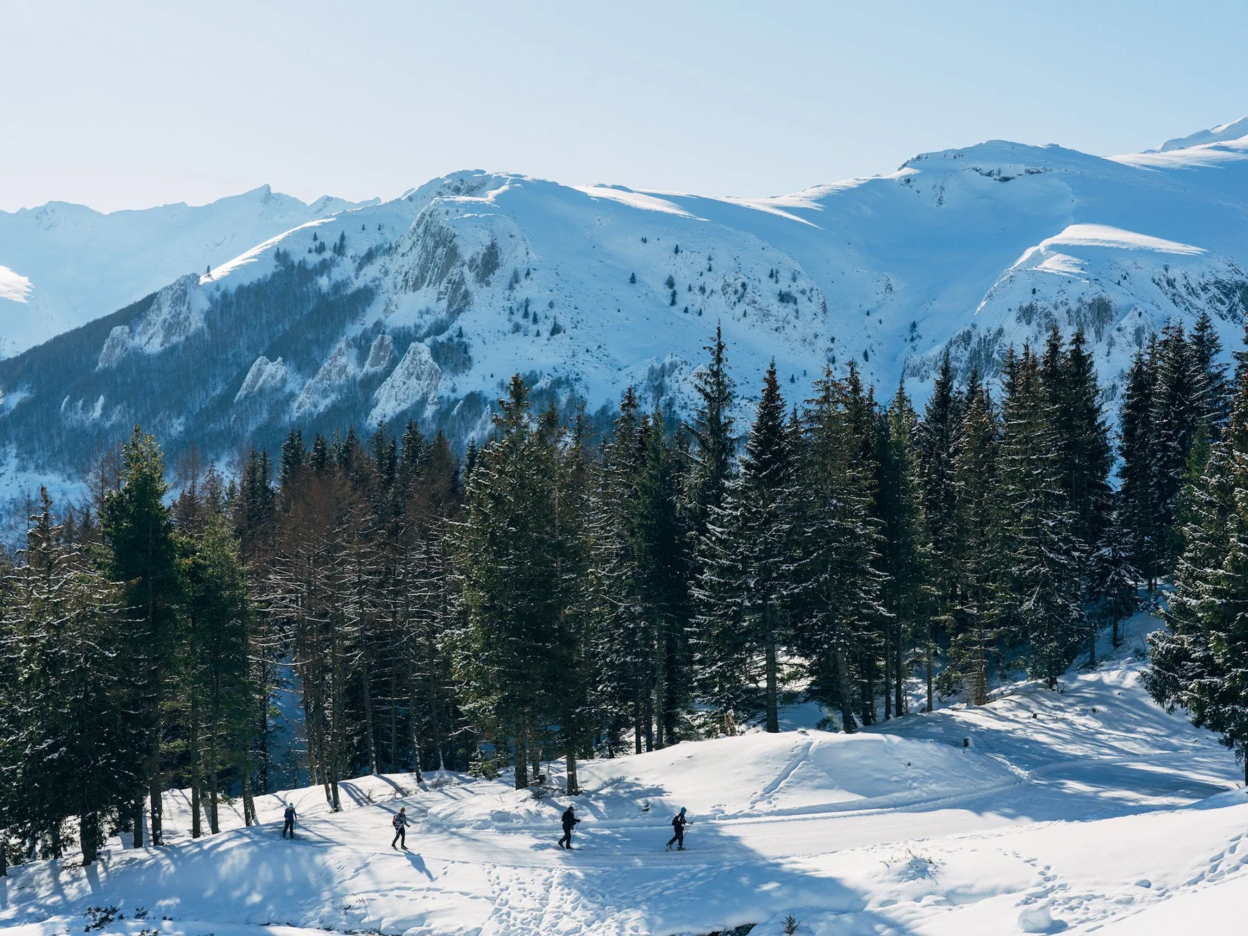 Paysage enneigé avec des montagnes, des arbres et des personnes faisant de la randonnée à raquettes.