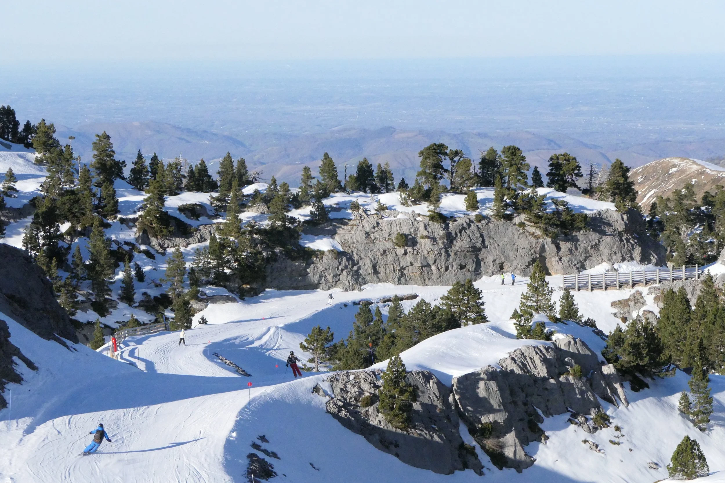 Pistes de ski enneigées avec quelques skieurs et arbres verts sur une montagne enneigée, vue lointaine du paysage.