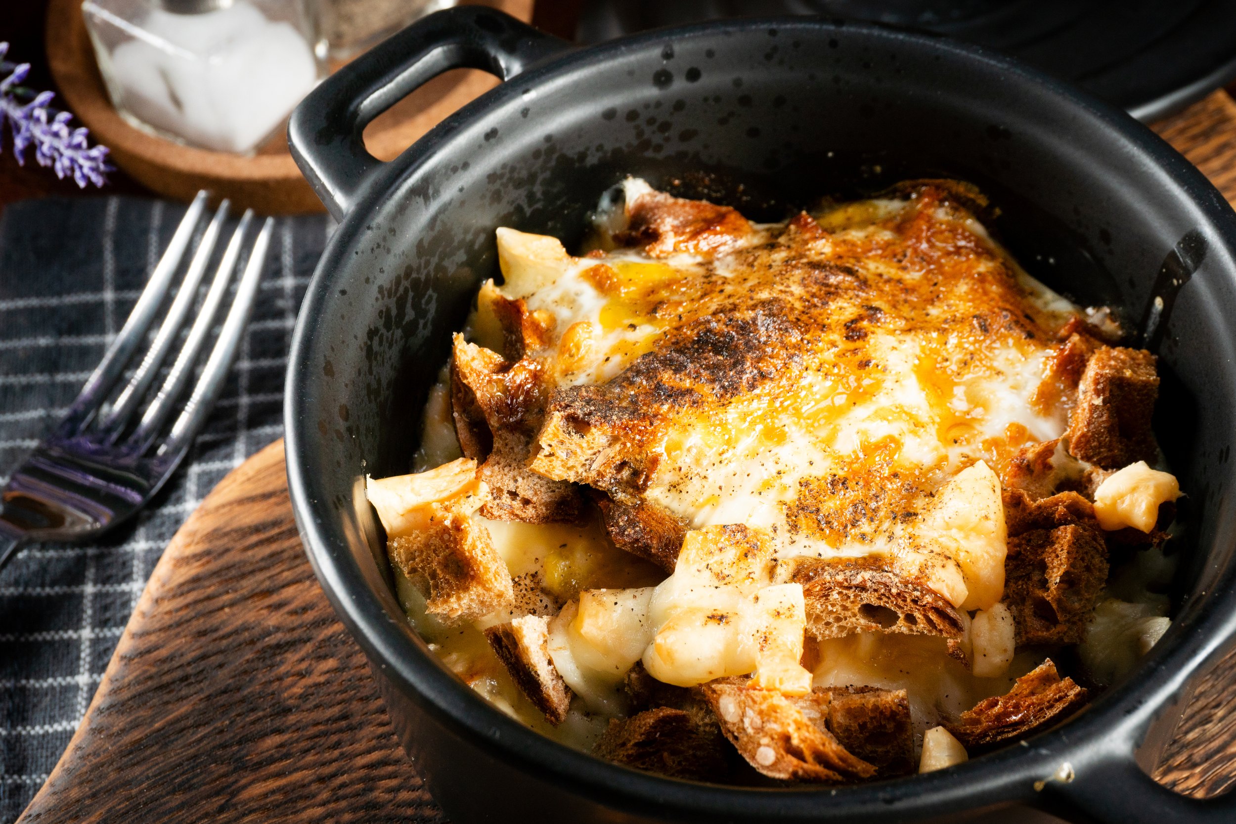 Gratin de pommes de terre avec fromage fondu, des morceaux de pain grillé et une surface dorée, servi dans un plat en fonte.