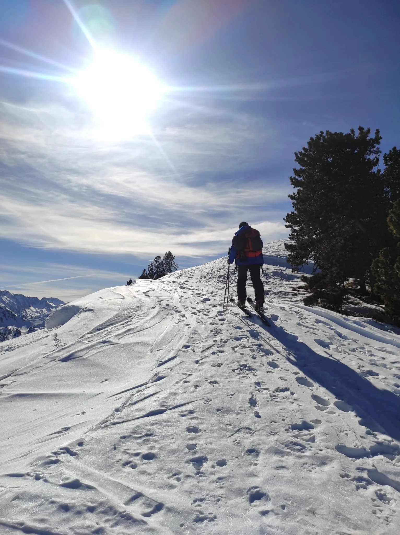 Une personne fait de la randonnée en ski de randonnée en montagne enneigée sous un ciel ensoleillé avec quelques nuages.
