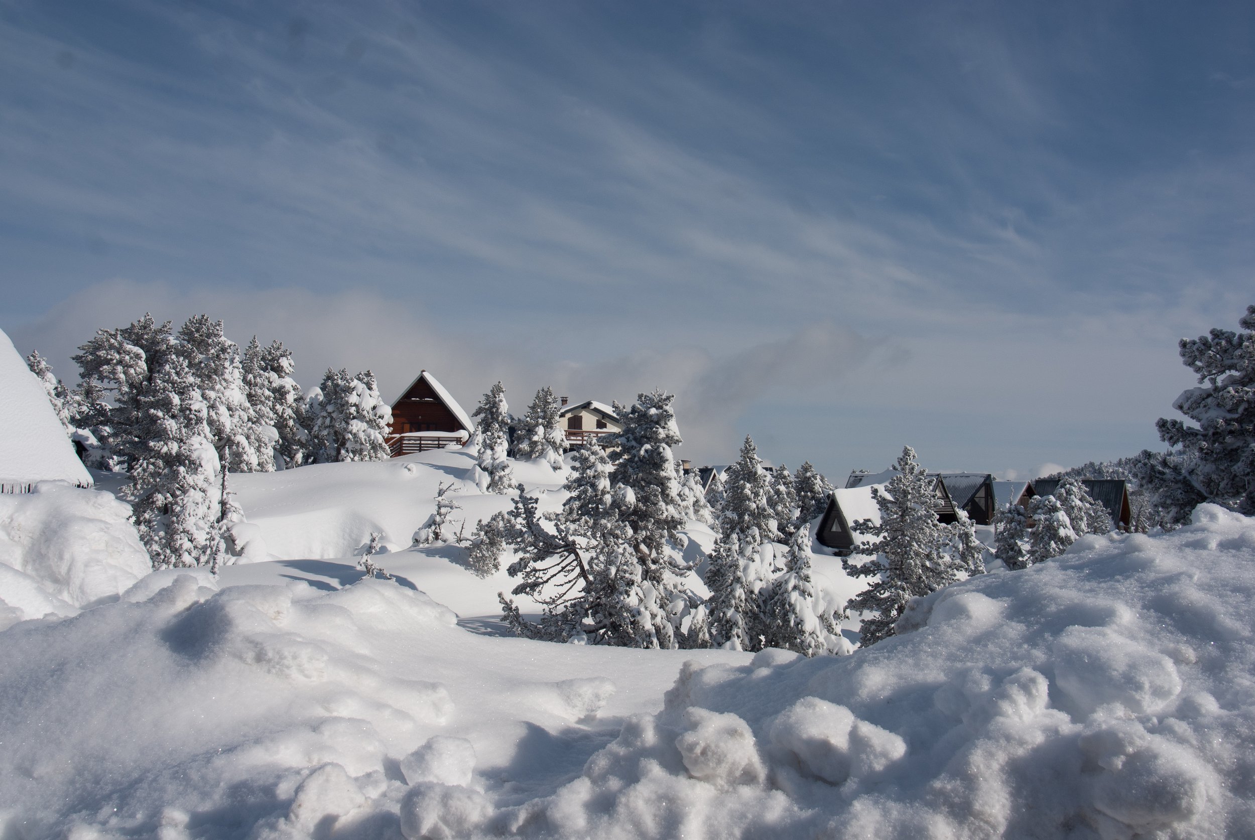 Village enneigé avec maisons, arbres recouverts de neige et ciel bleu avec quelques nuages.
