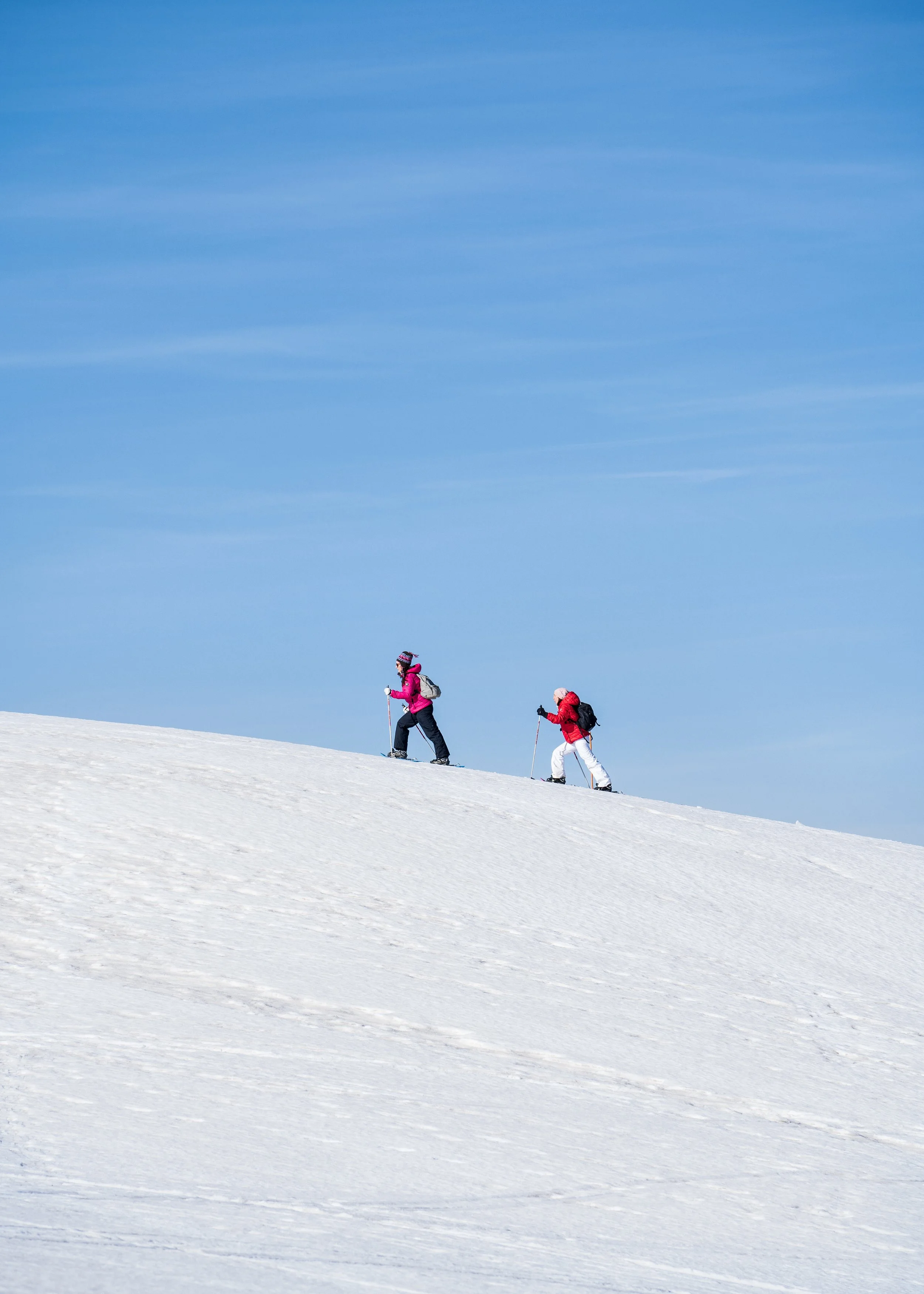 Deux personnes font de la randonnée en ski de randonnée sur une pente enneigée sous un ciel bleu.
