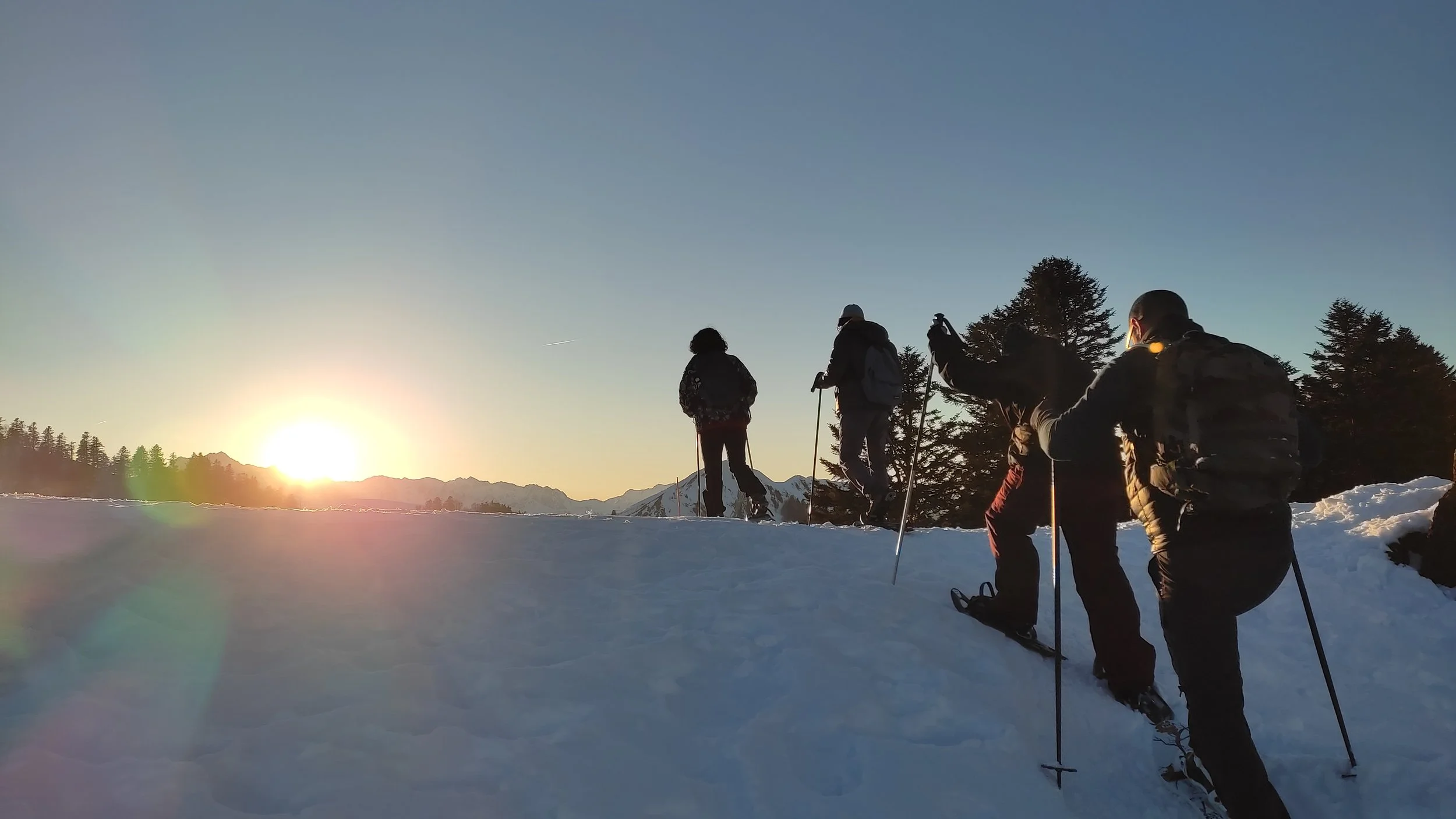 Groupe de personnes faisant de la randonnée en raquettes sur neige au coucher du soleil dans un paysage montagneux.