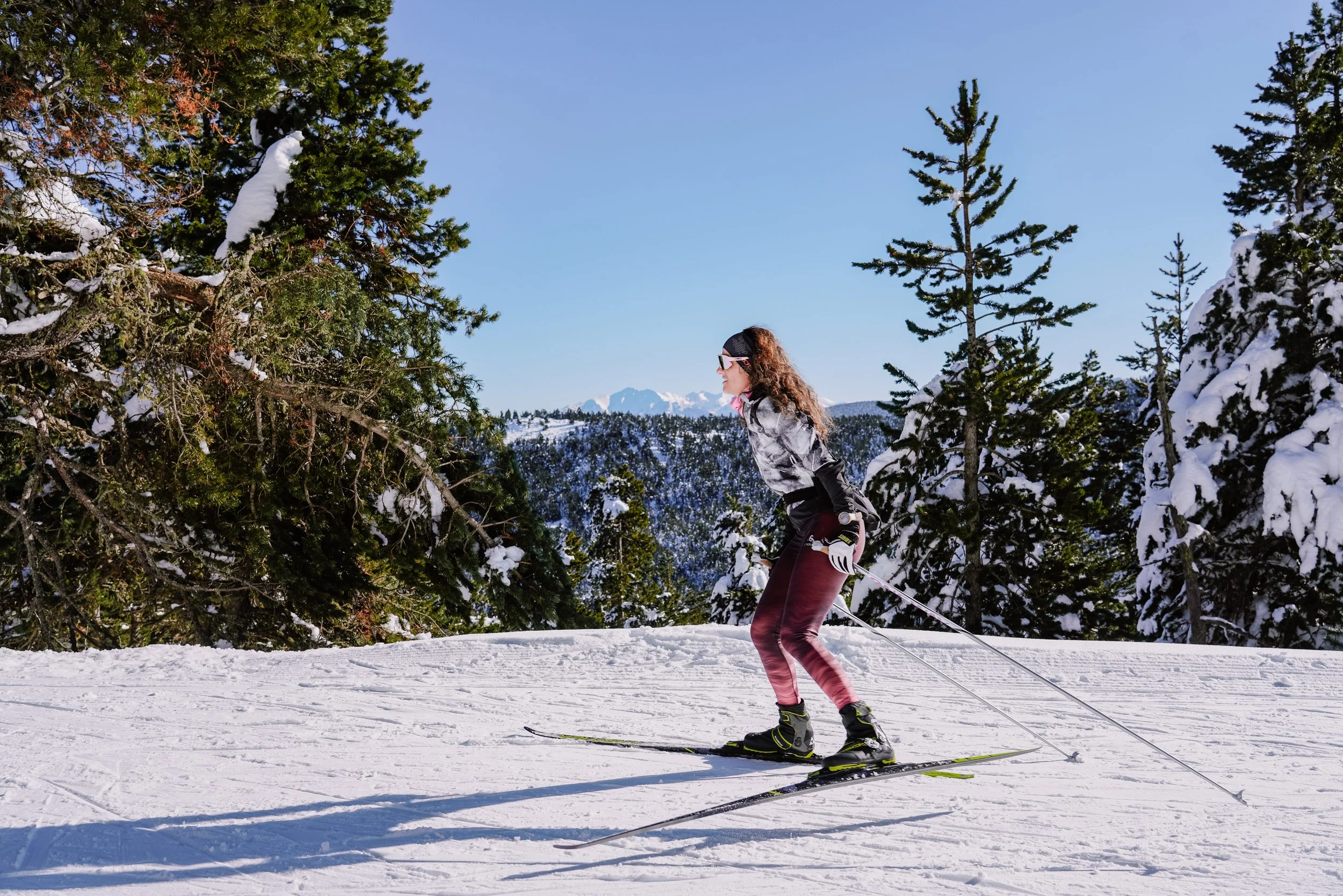 Femme faisant de la ski dans une forêt enneigée en montagne avec un ciel bleu clair.