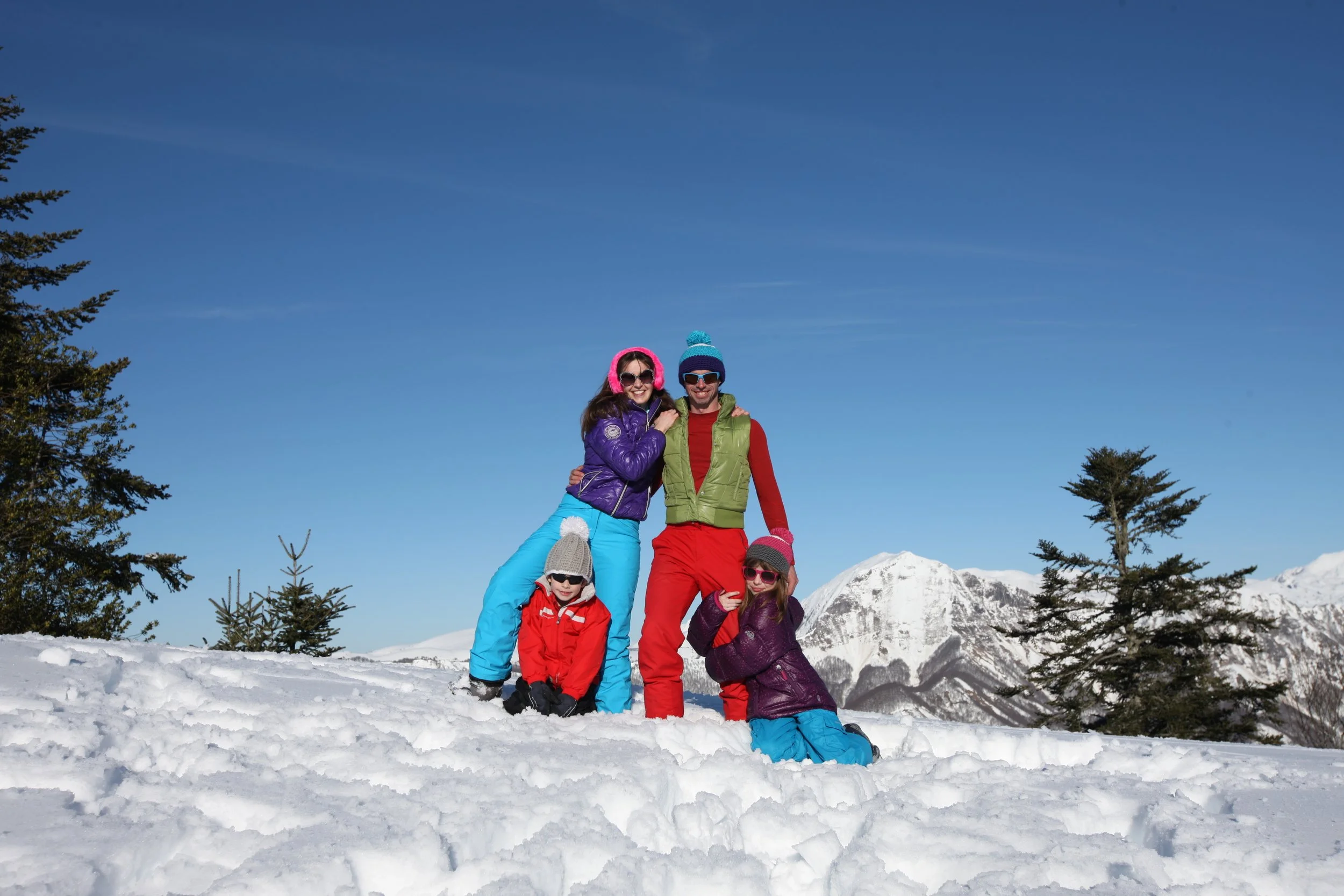 Une famille de cinq personnes en vêtements d'hiver, souriant dans un paysage enneigé avec des montagnes en arrière-plan