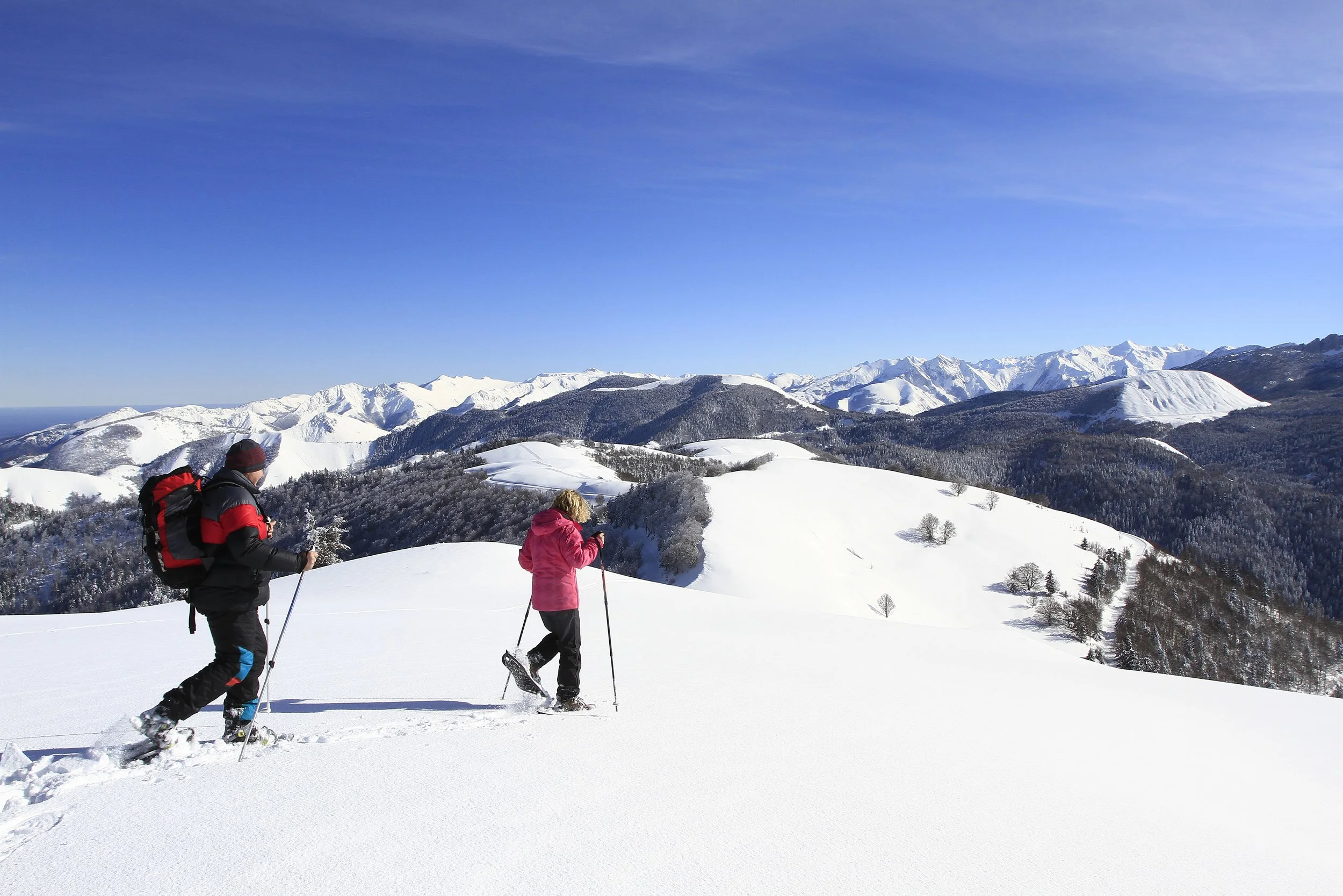 Deux personnes faisant de la randonnée en raquettes dans un paysage enneigé avec des montagnes en arrière-plan.