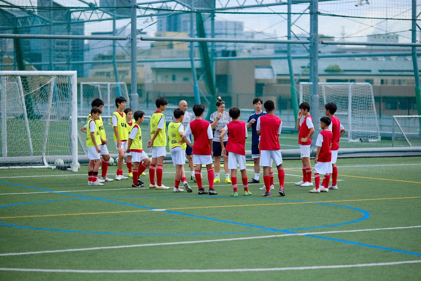 サッカーの練習を行う子供たちとコーチ。中央にコーチがいて、子供たちが円になって立っている。