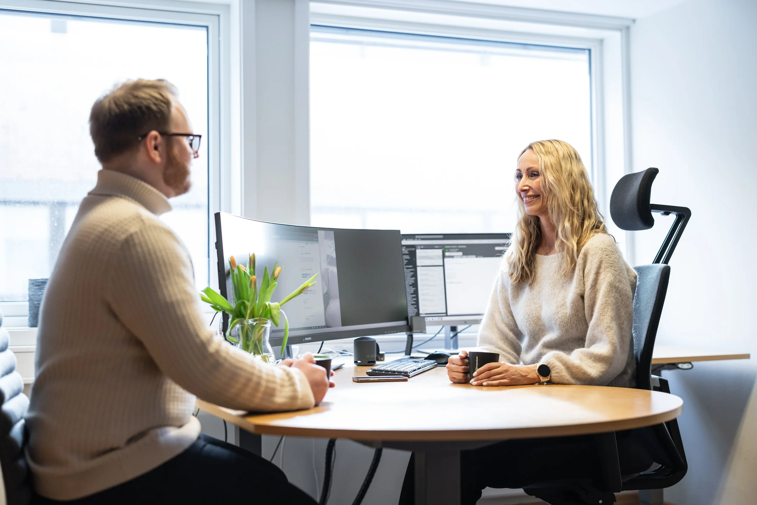 To personer sitter ved et bord og har en samtale, en kvinne med blondt hår og en mann med briller og mørkt hår.