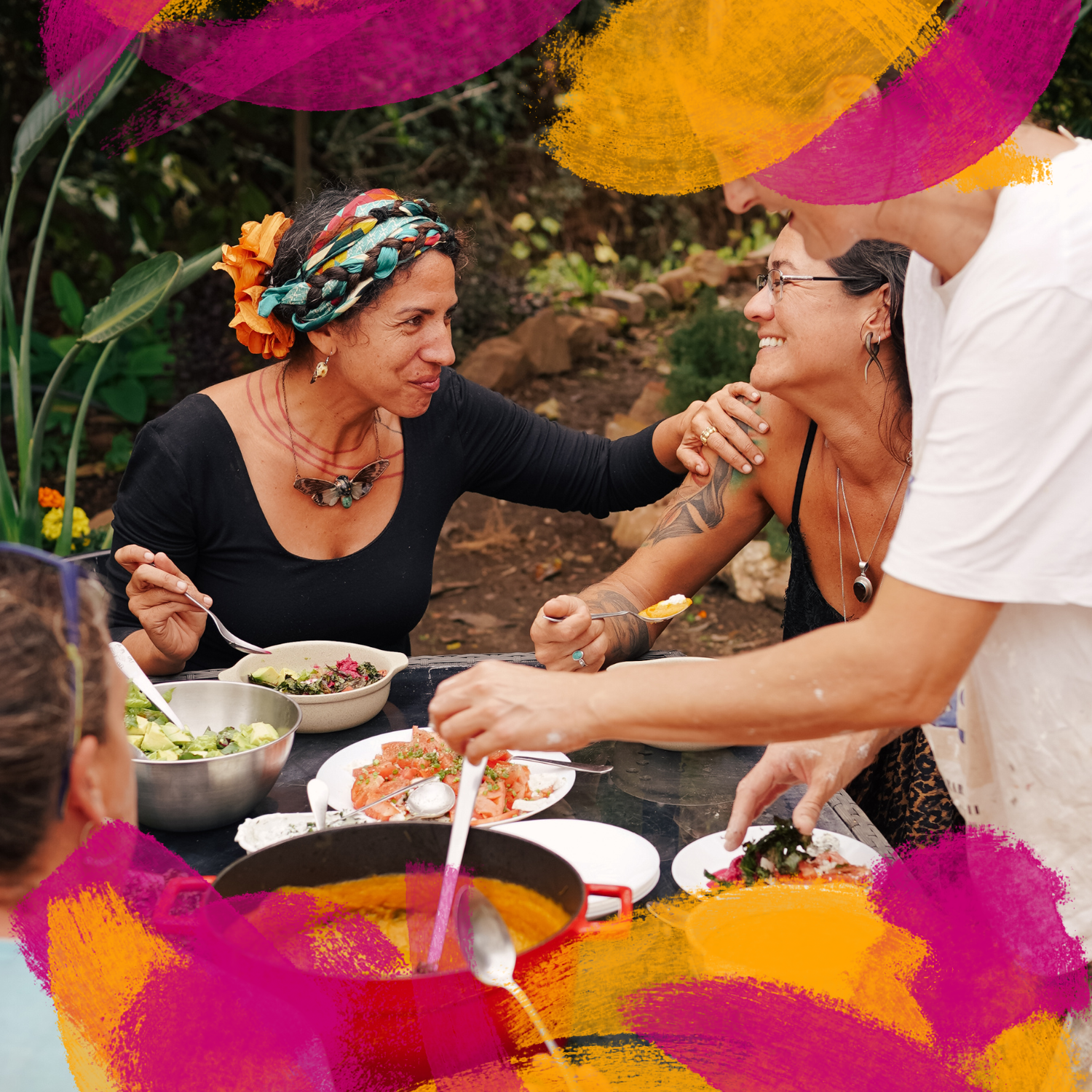 Group of women sharing a meal outdoors, embracing and smiling, surrounded by colorful painted brush strokes.