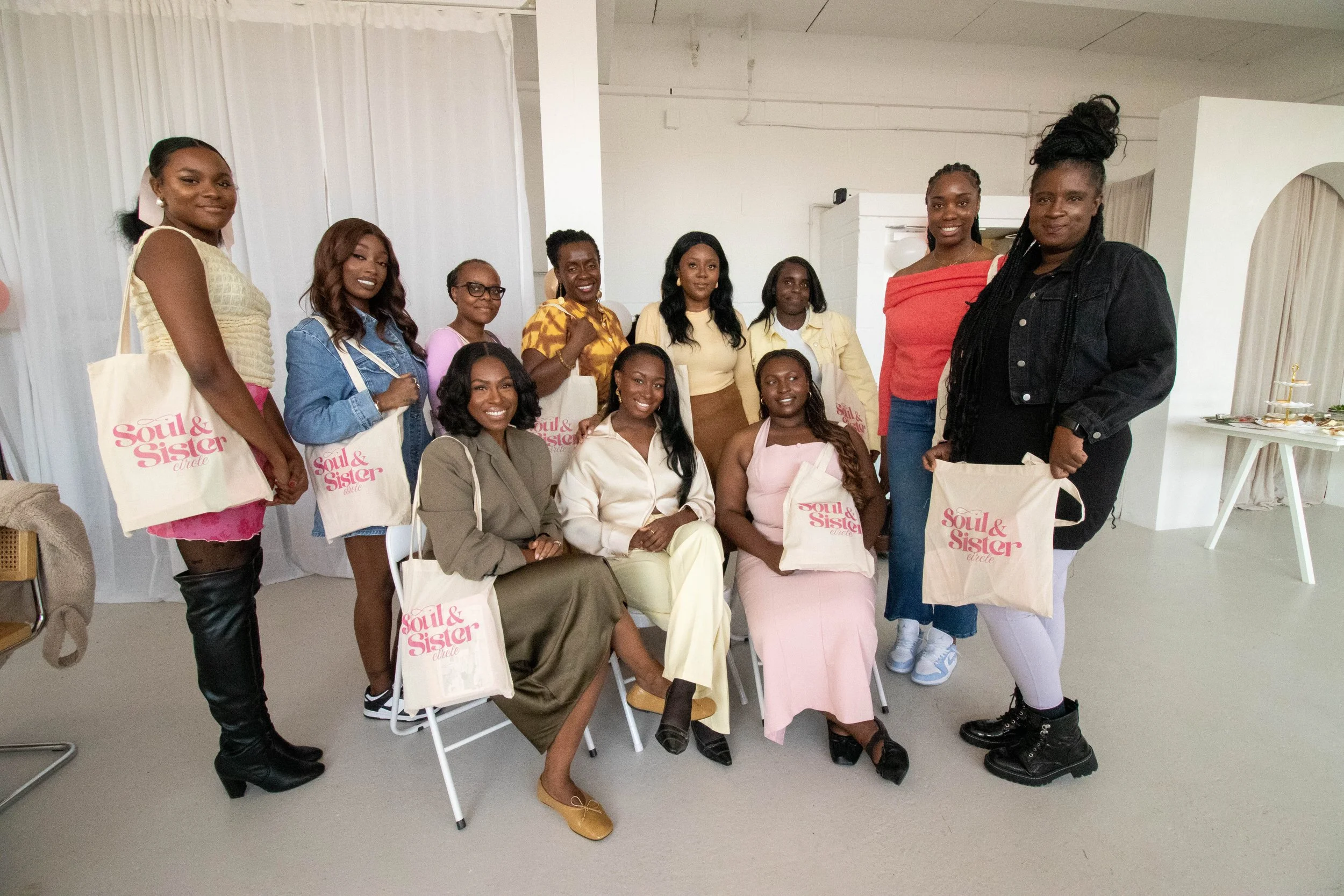A group of women posing for a photo at an indoor event, holding tote bags that read 'Soul & Sister Circle.'