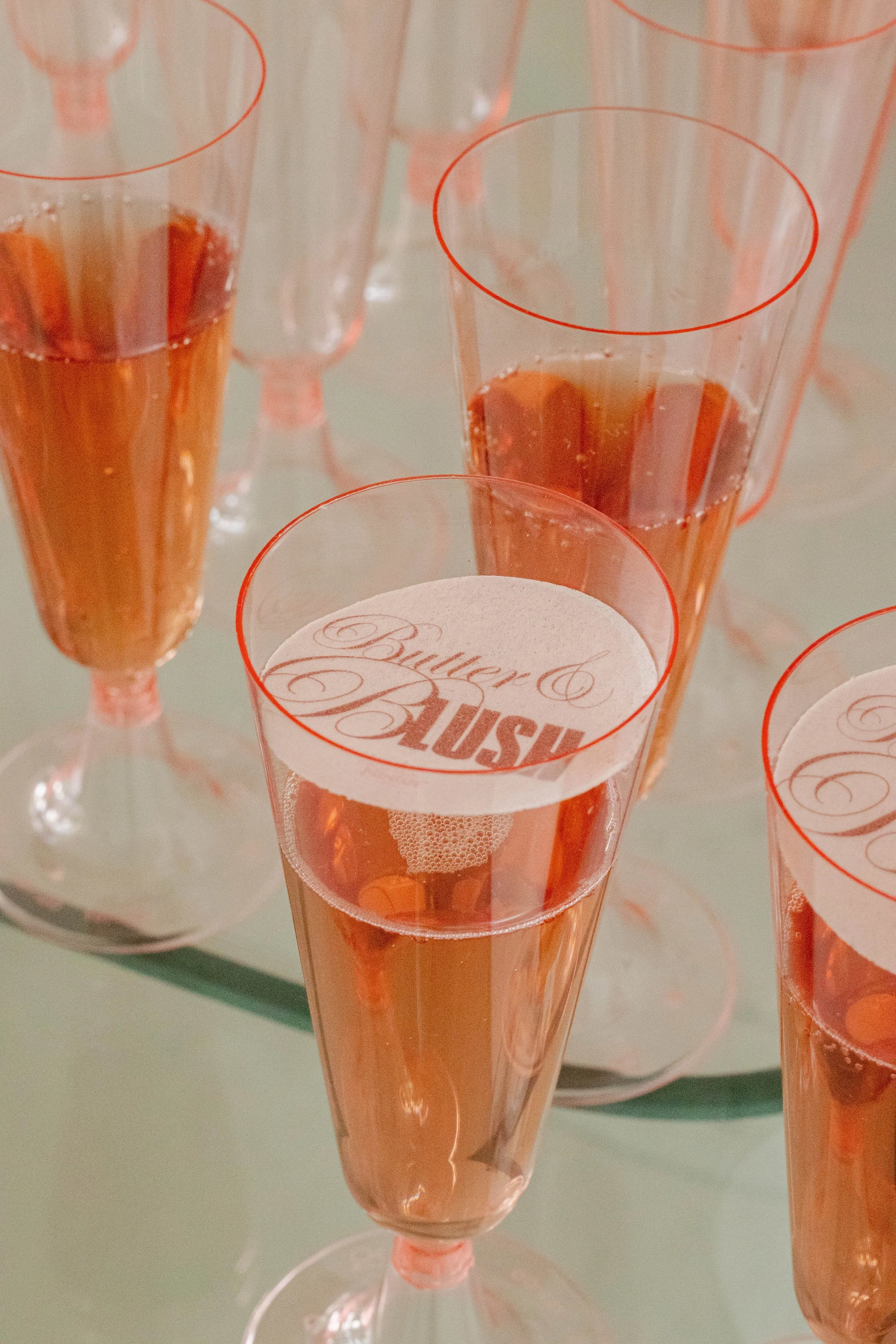 Champagne glasses with pink-colored bubbly drink and a 'Buyer & Hussy' logo on the top of the glass.