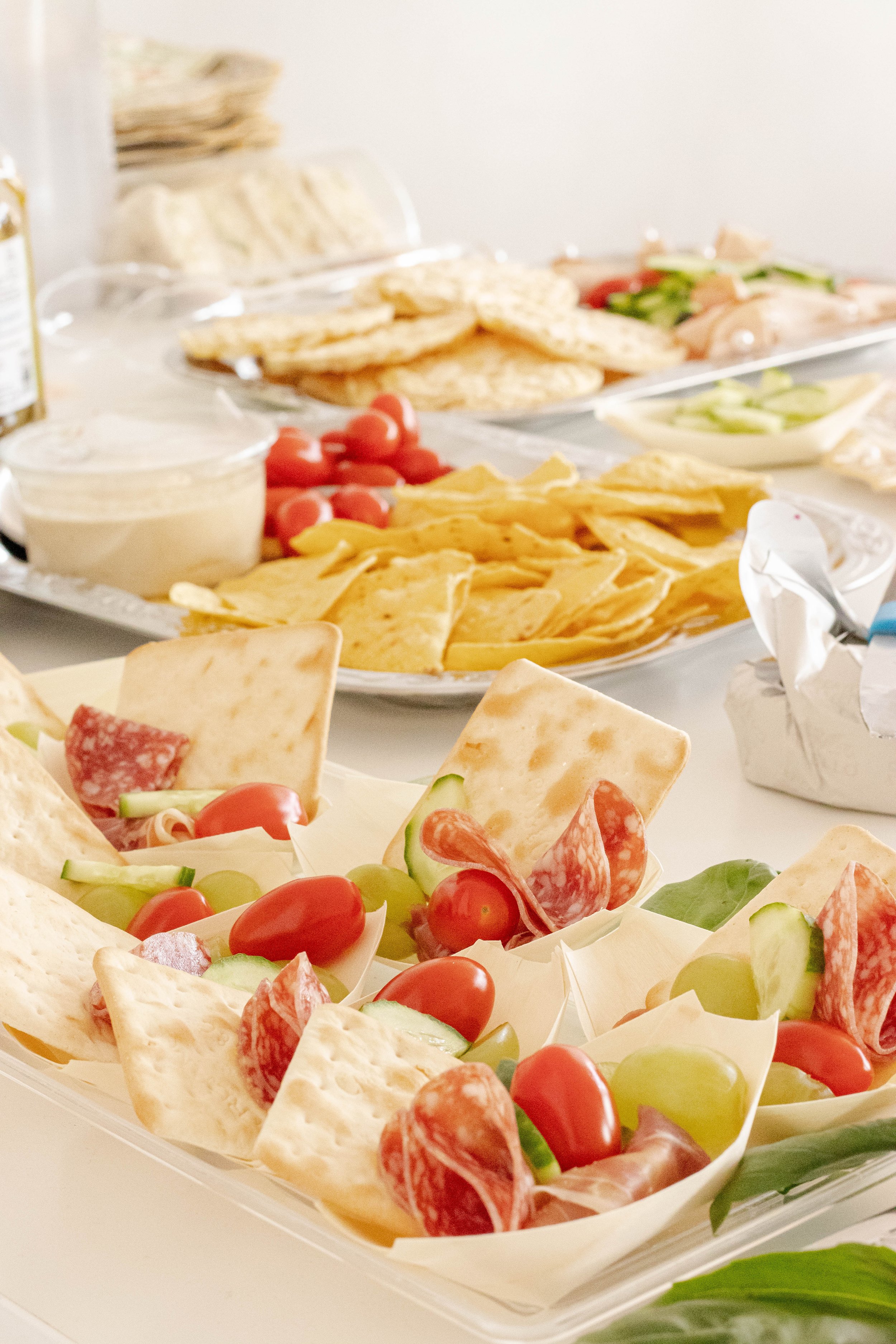 Tray of individual appetizer cups filled with grape tomatoes, slices of cucumber, salami, and cheese, garnished with lettuce.