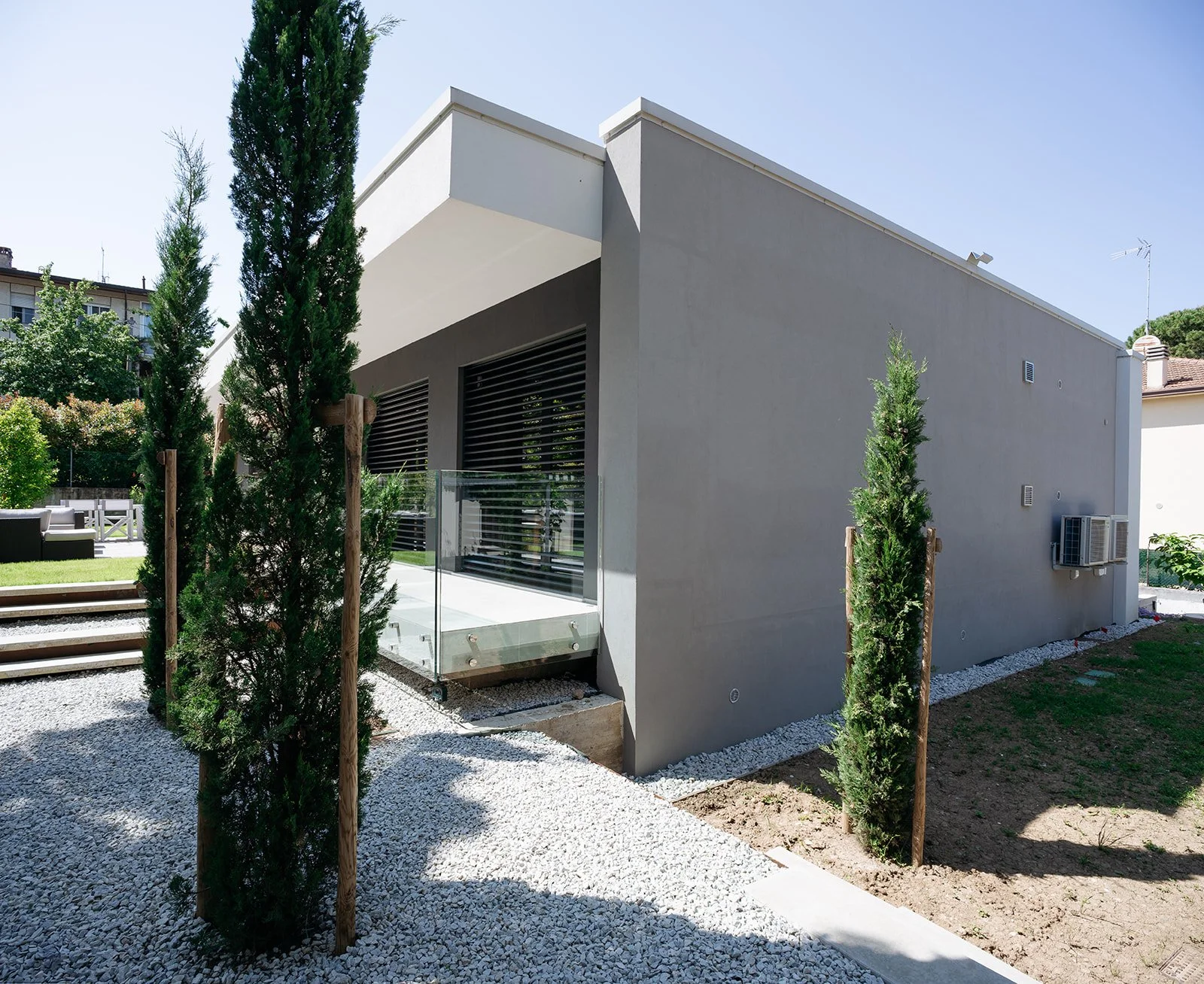 Facciata laterale di villa moderna minimalista con rivestimento grigio e giardino, progetto DAT Architetti.