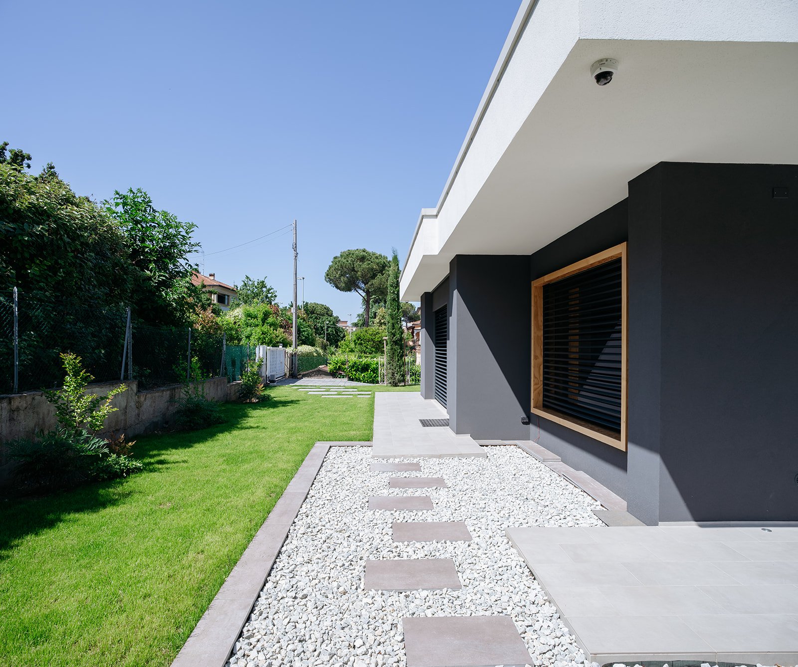 Percorso esterno pavimentato con vista sulla facciata laterale di villa moderna, DAT Architetti.