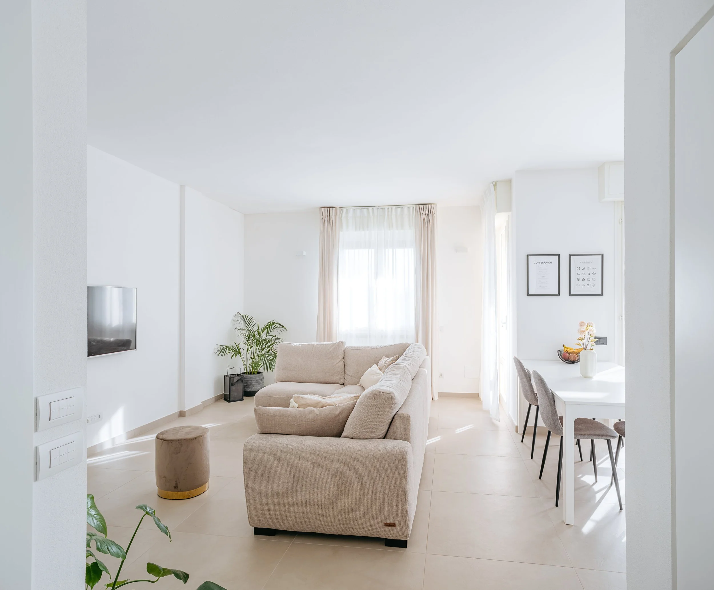 Soggiorno luminoso con divano beige e cucina a vista.