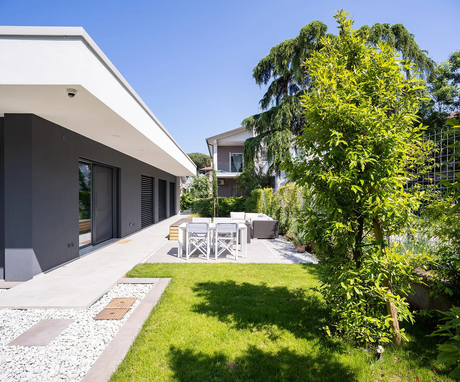 Giardino di villa minimalista con pavimentazione in pietra bianca e facciata grigio antracite, DAT Architetti.