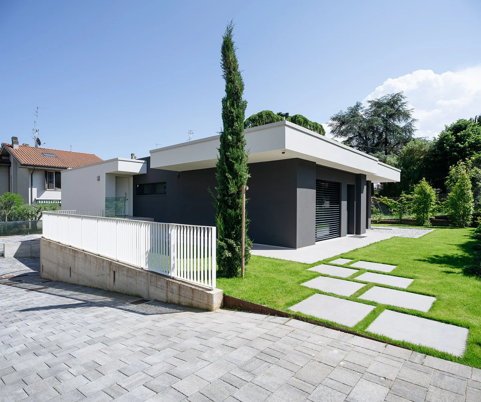 Ingresso principale di villa moderna con recinto bianco e giardino curato, progetto DAT Architetti.
