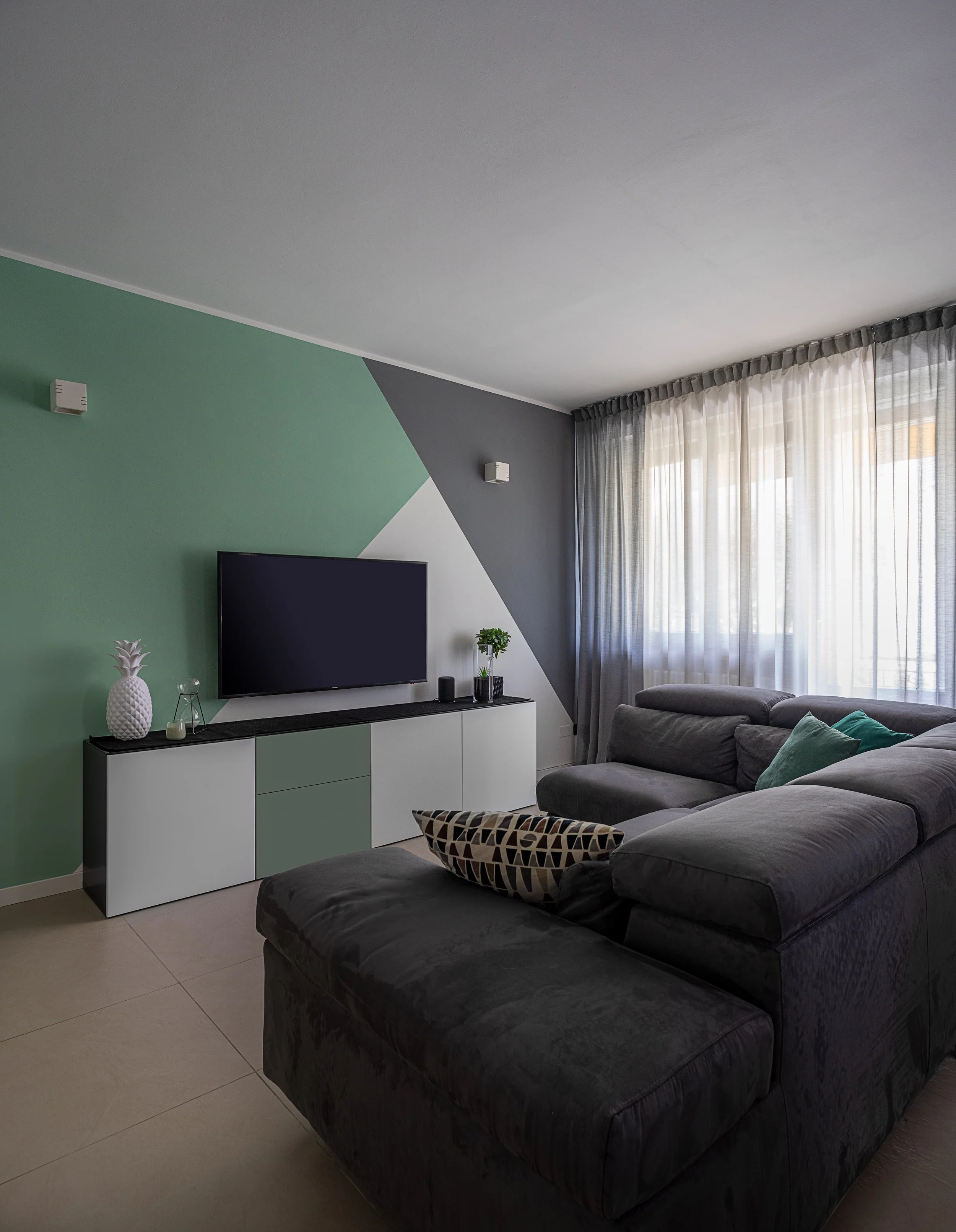 Zona giorno con parete verde salvia e divano grigio, progetto residenziale.