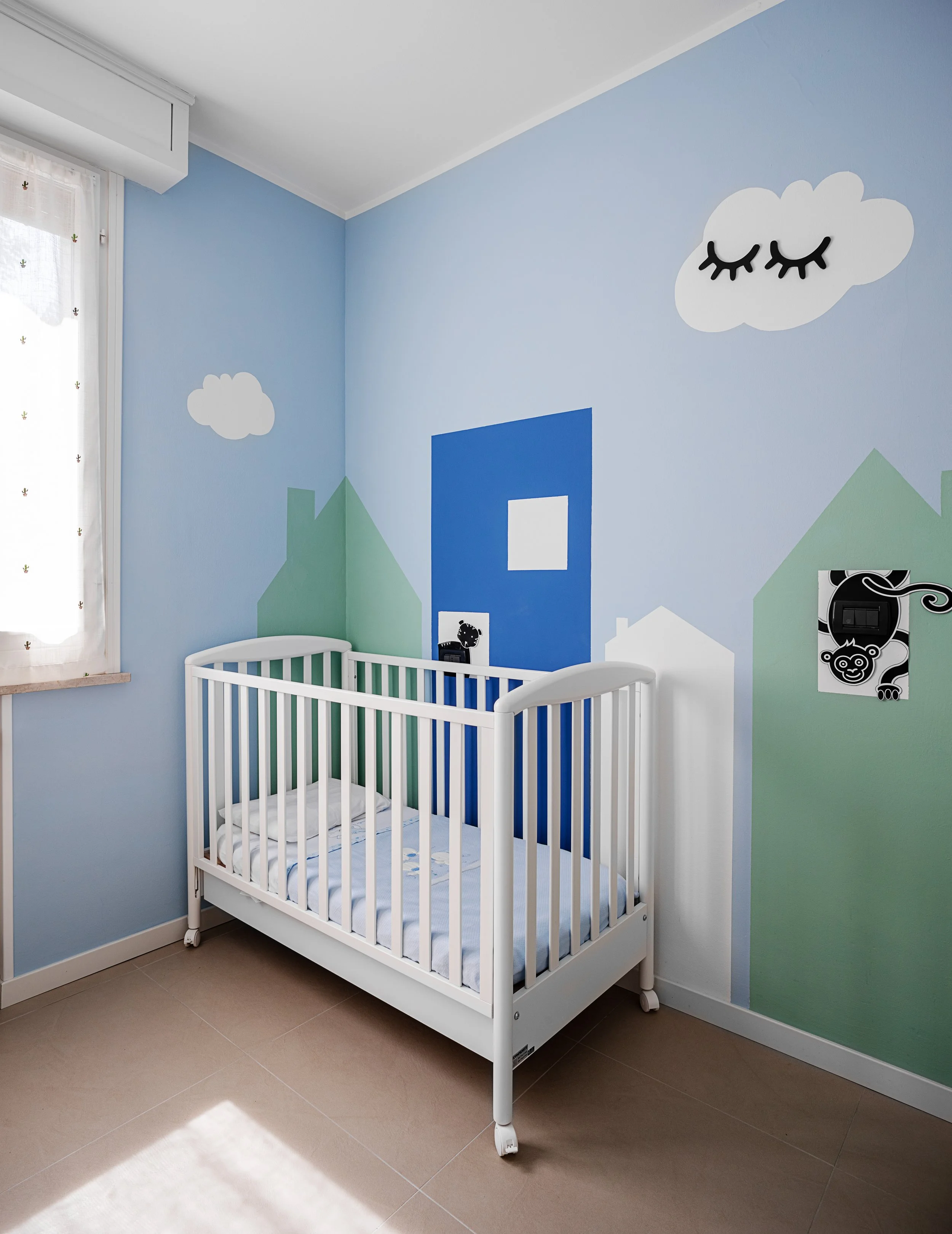 Cameretta con parete decorata a tema casette e colori pastello.