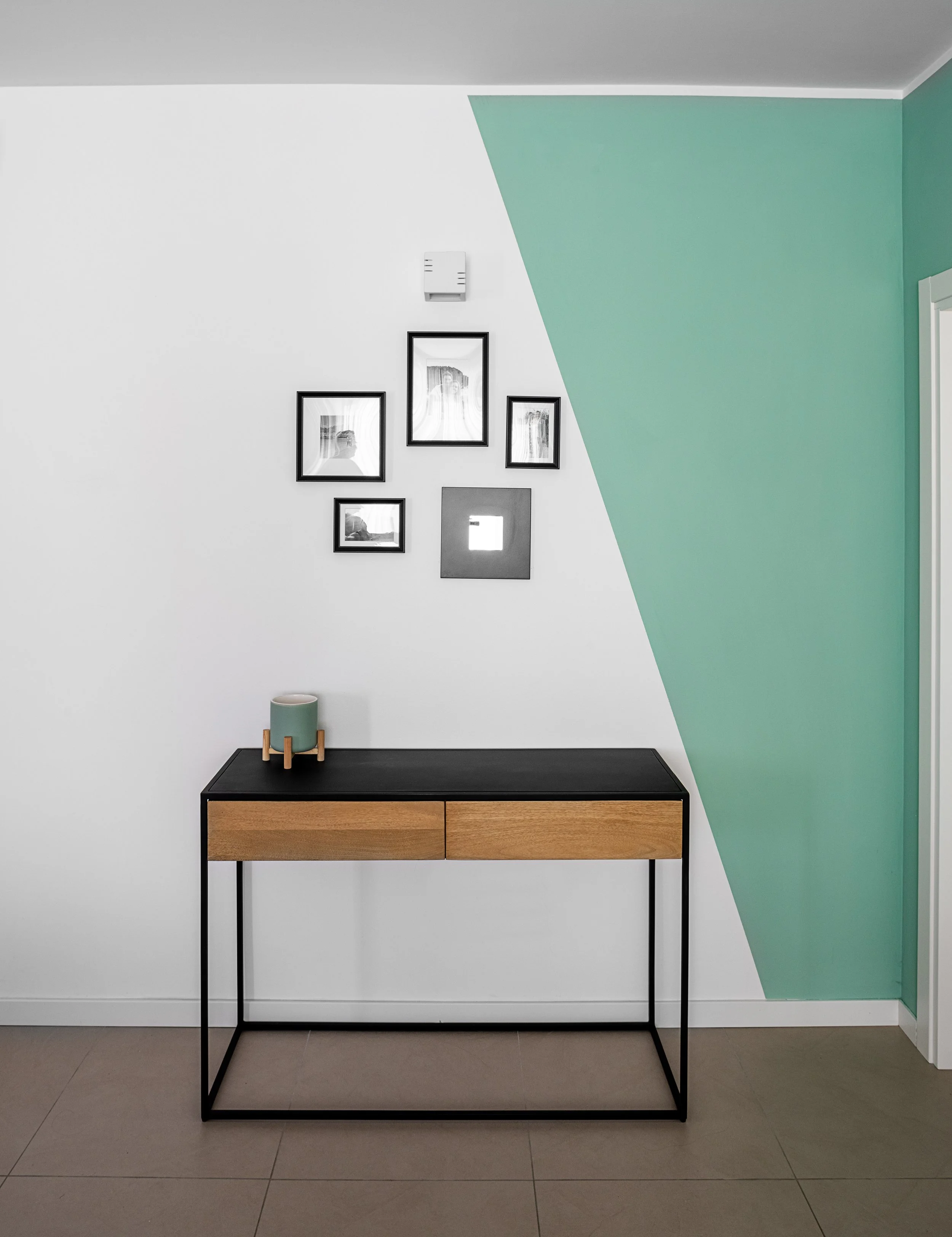  Ingresso con parete verde salvia e consolle in legno e metallo nero.