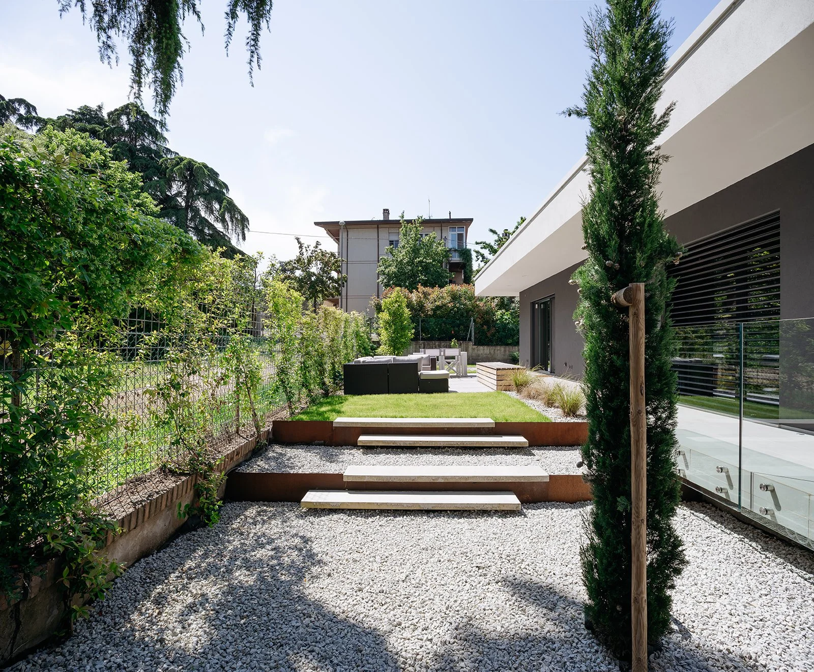 Prospetto di villa contemporanea con giardino in ciottoli e cipressi, progettata da DAT Architetti.