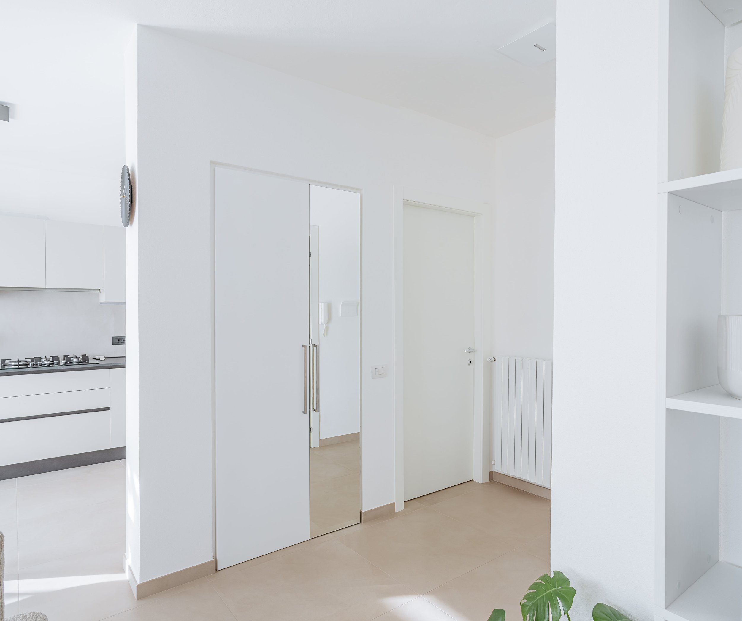 Dettaglio ingresso con porta a specchio e pareti bianche.