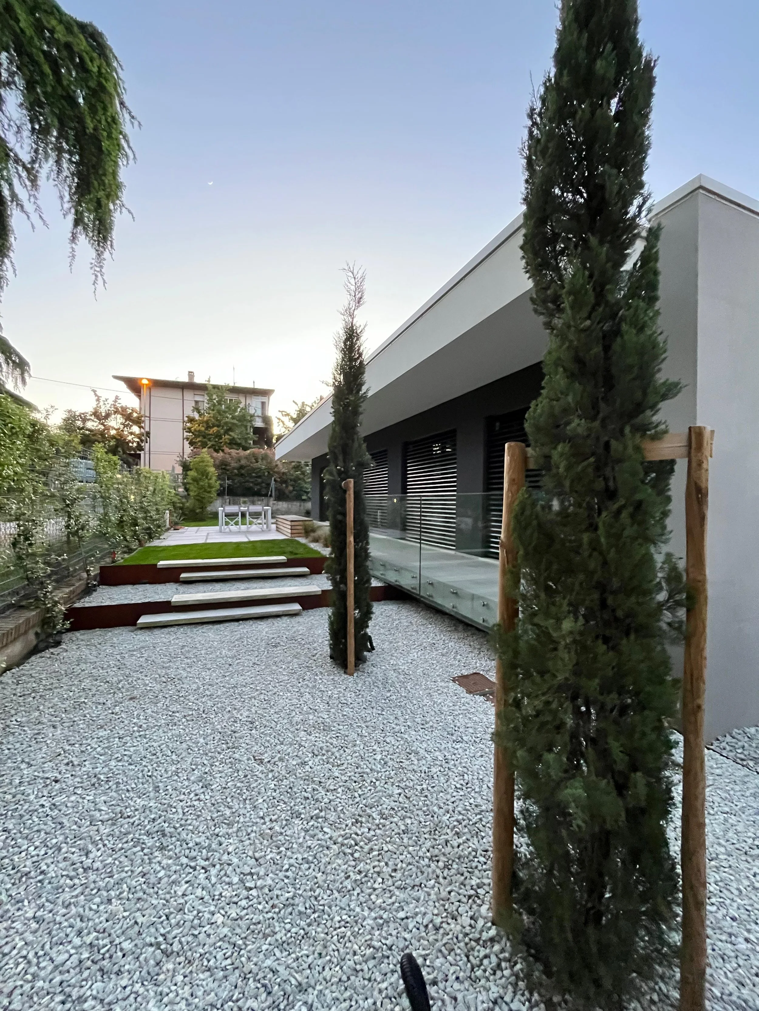 Cortile di villa contemporanea con pavimentazione in ghiaino bianco e cipressi. Dettagli di architettura pulita e materiali di qualità, DAT Architetti.
