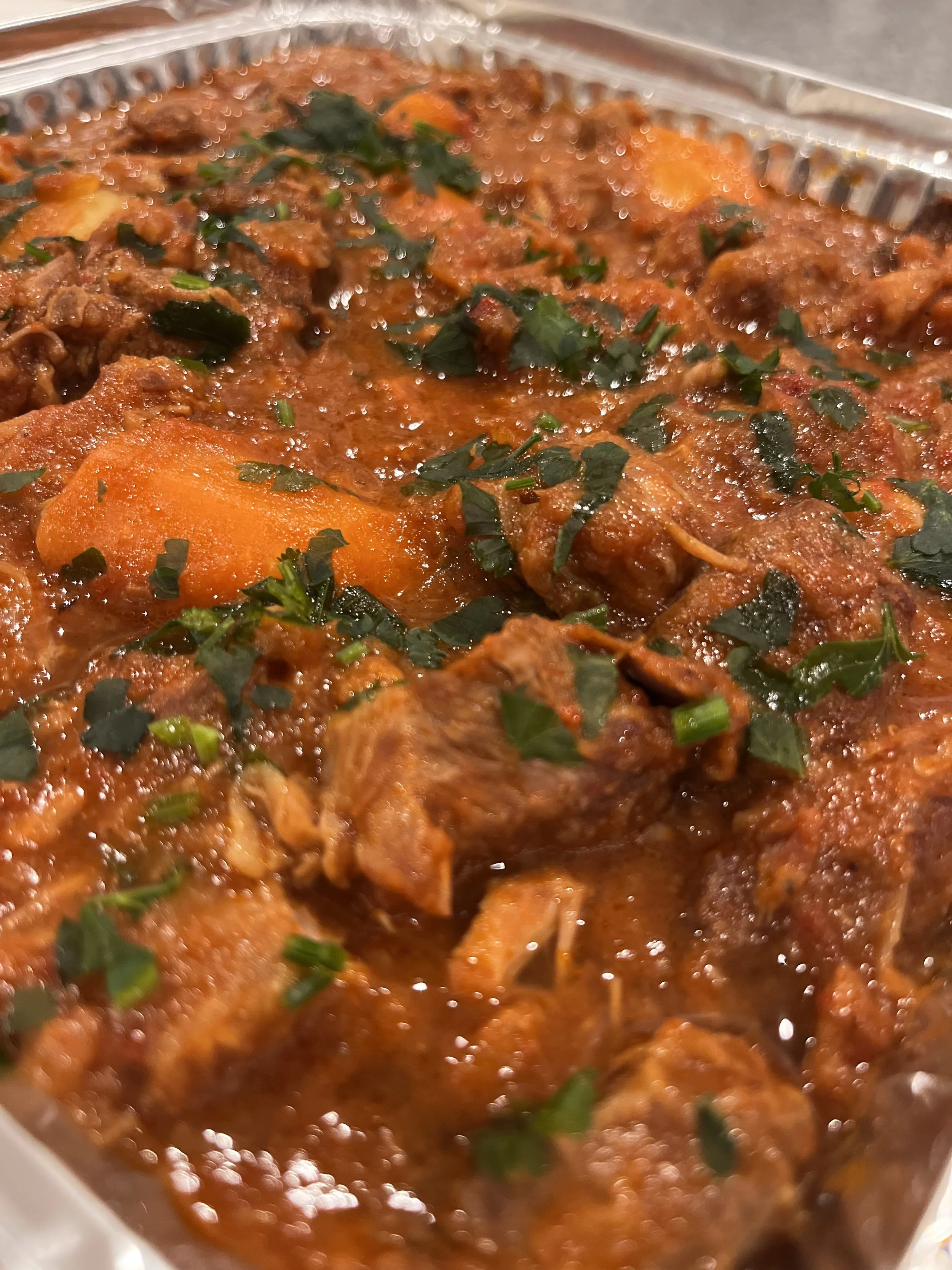 Close-up of a beef stew with carrots and herbs in a metal tray.