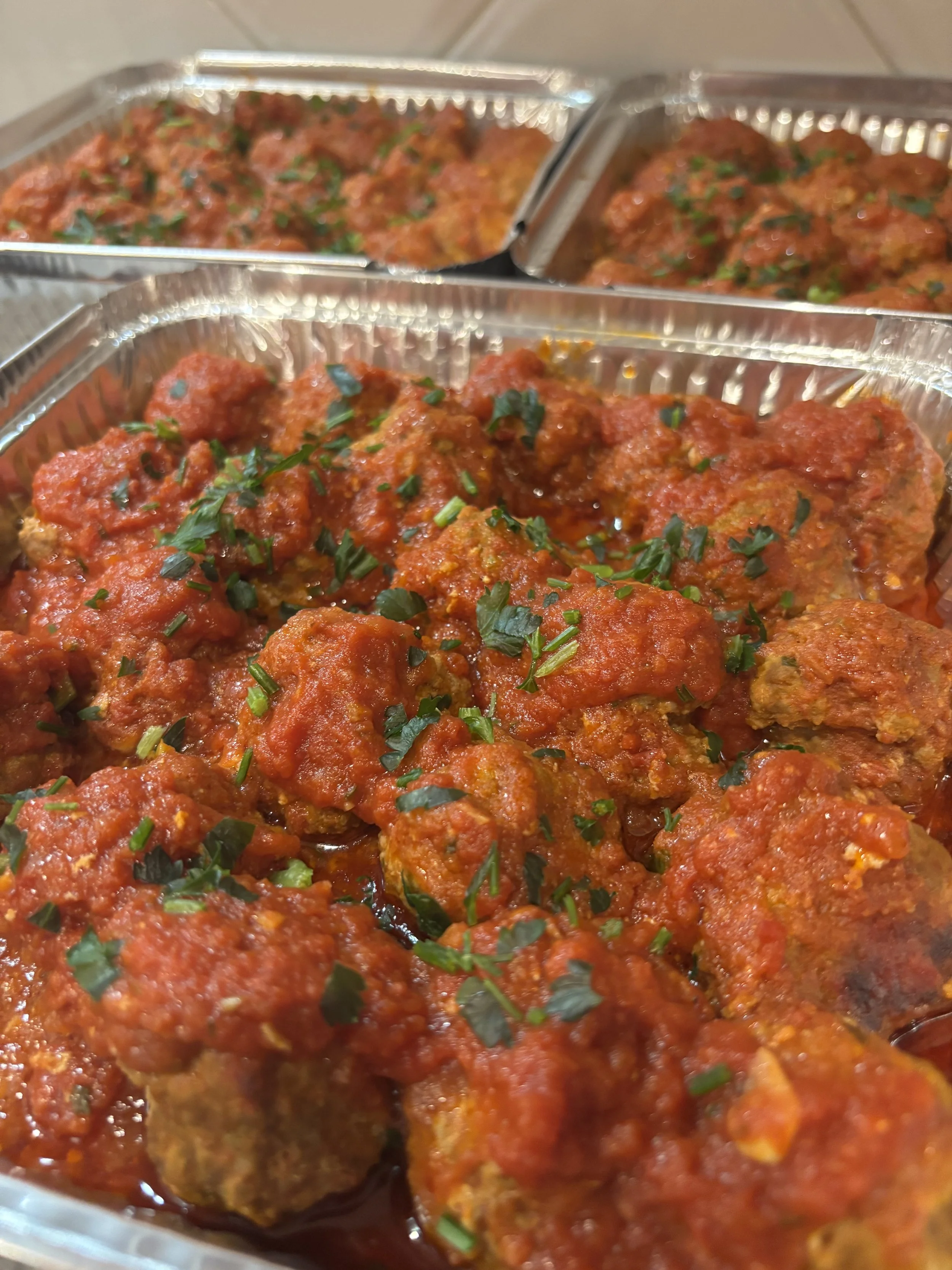 Tray of cooked Italian meatballs in tomato sauce, garnished with chopped fresh herbs.