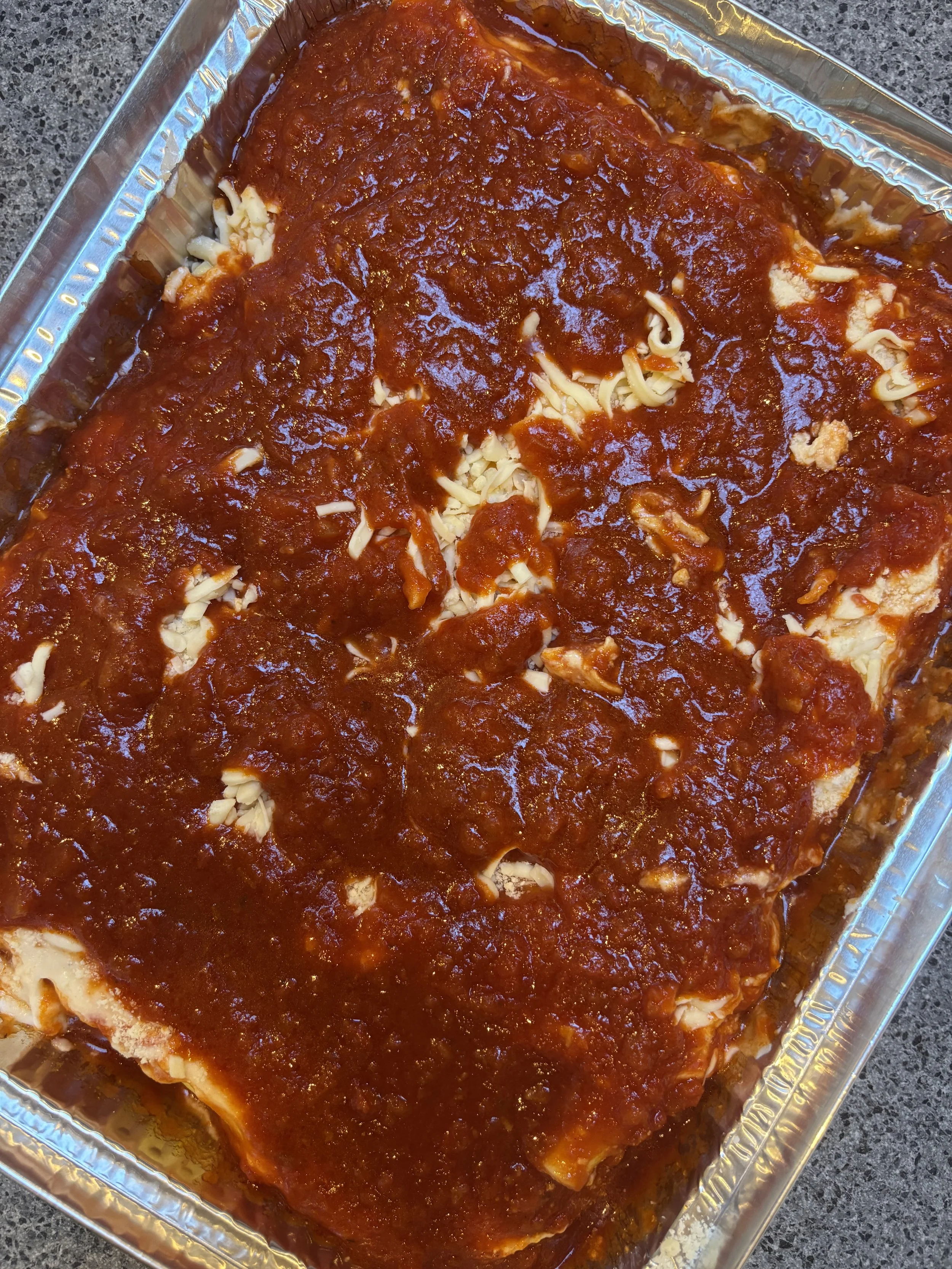 Unbaked lasagna in a silver baking dish with pasta, meat, cheese, and tomato sauce