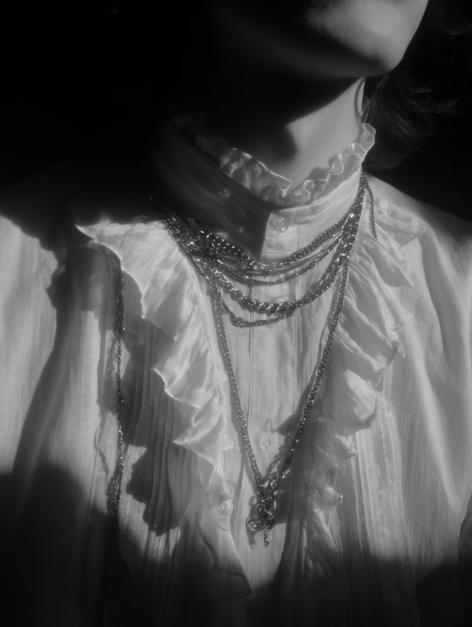 Überbelichtetes Bild von Silberketten an einer Person, die ein Rüschenhemd trägt