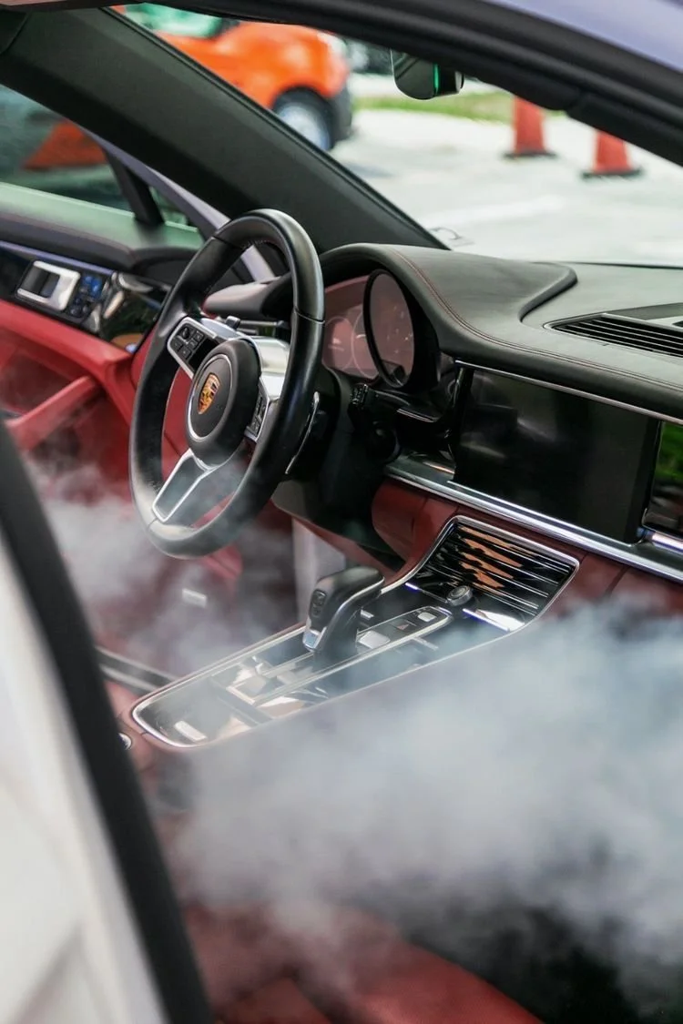 Interior of a Porsche car with a steering wheel, dashboard, and gear shift, seen through a foggy window.