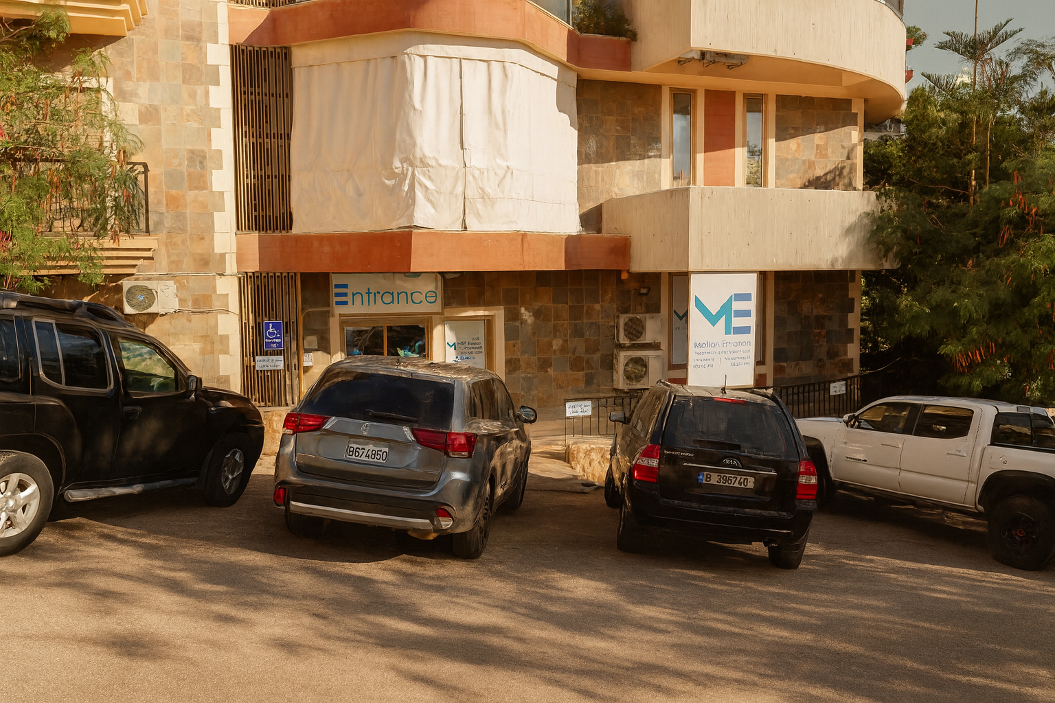 Building entrance with four parked cars in front, including a black SUV, a gray SUV, a black hatchback, and a white pickup truck, with signs indicating entrance and disability parking.
