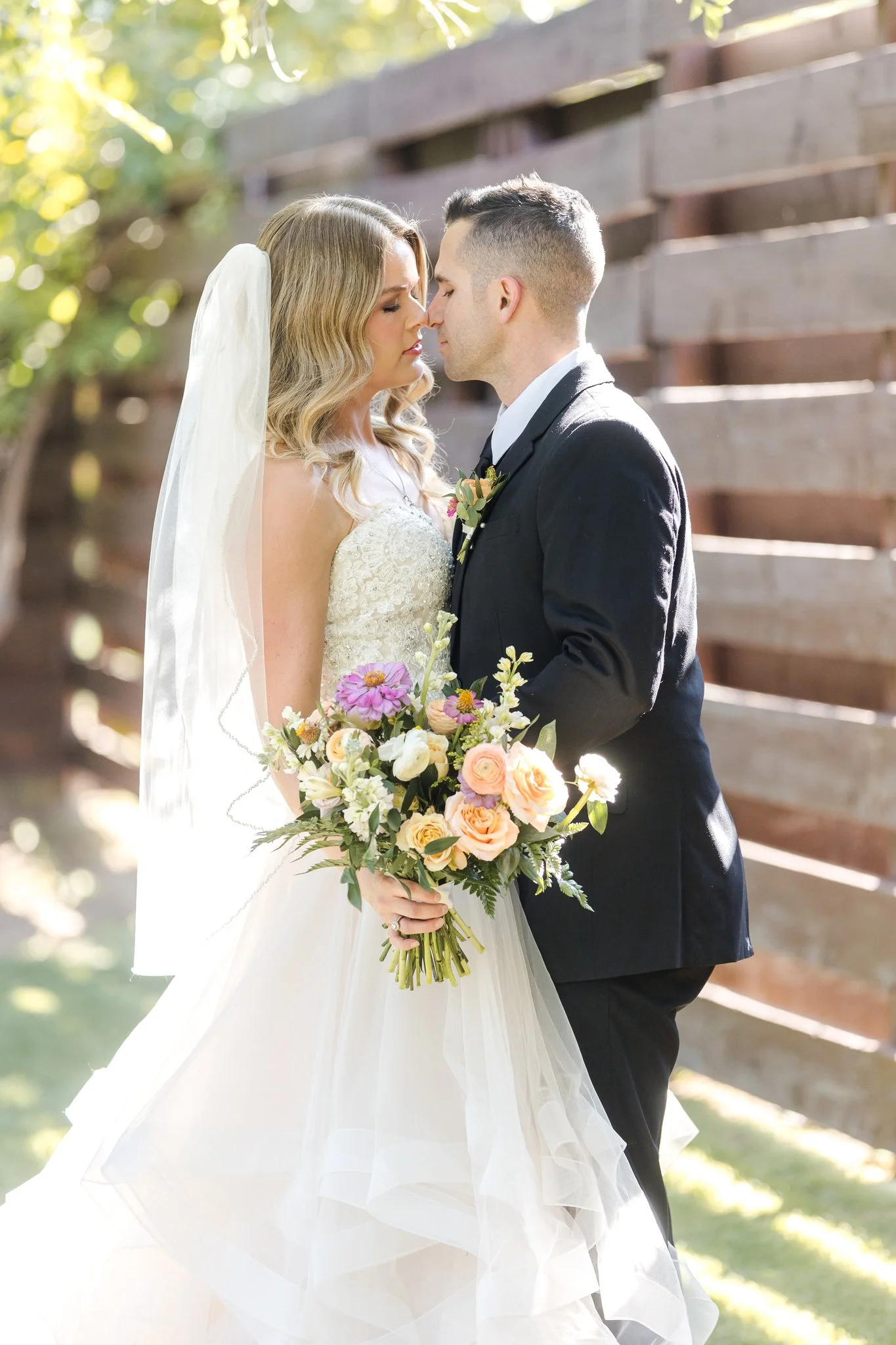 Bride and groom holding a colorful garden-style wedding bouquet with peach, pink, yellow and lavender flowers.