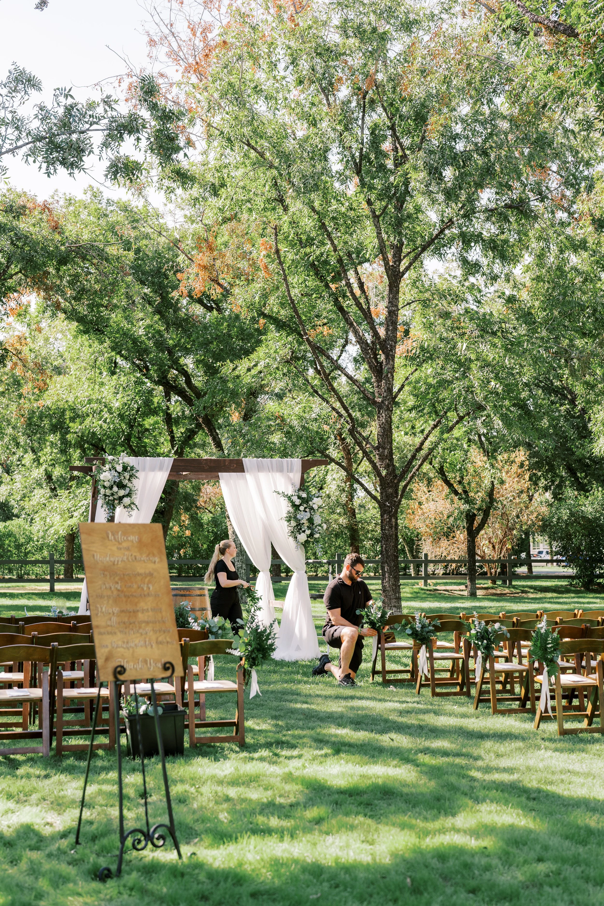 Tree-filled outdoor ceremony at Venue at the Grove with white draping, greenery and romantic garden wedding details.