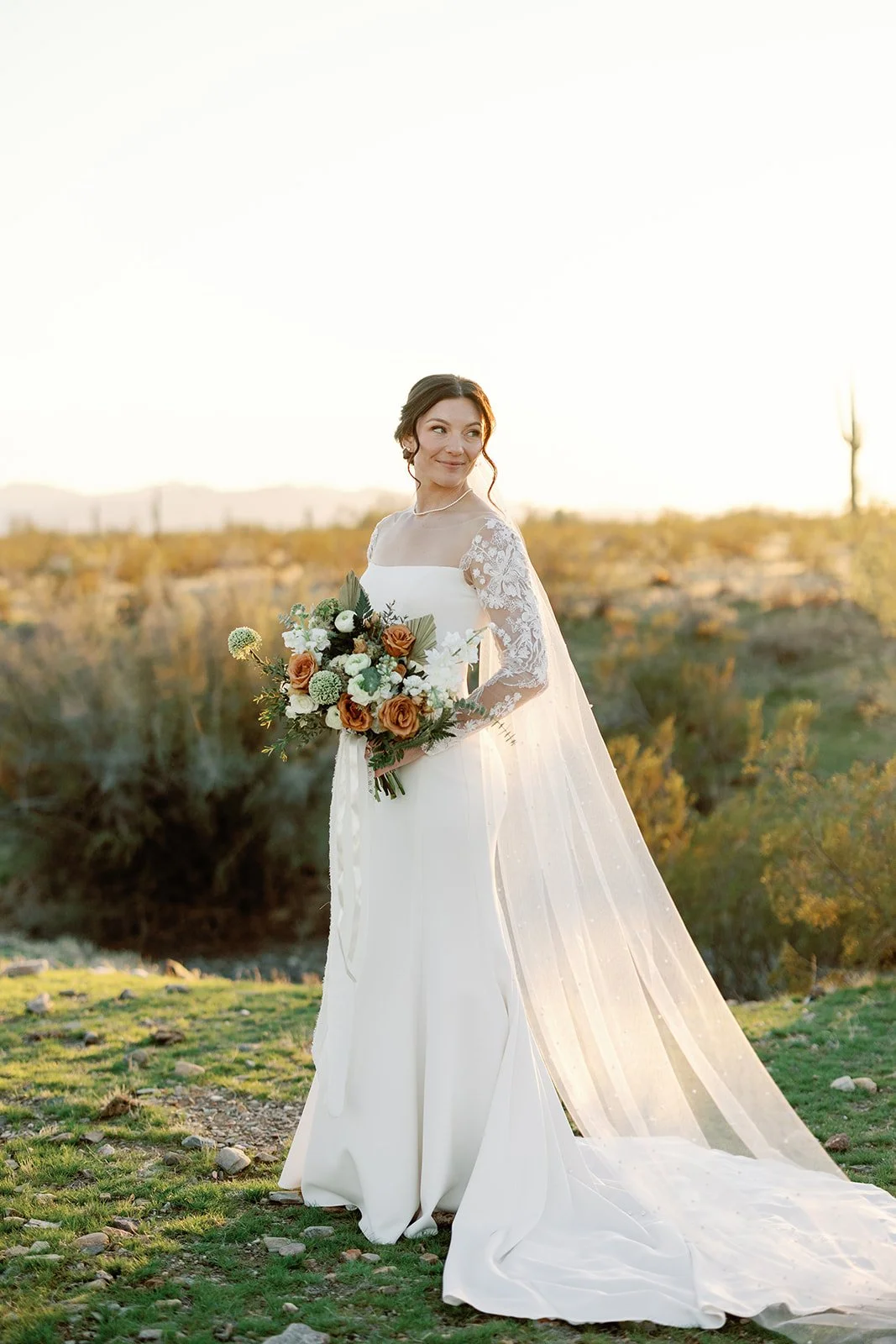 Bride standing outdoors at sunset holding a romantic garden-style wedding bouquet.