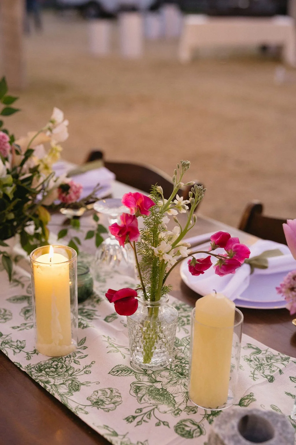 Romantic backyard wedding table with colorful bud vases, bright flowers and glowing pillar