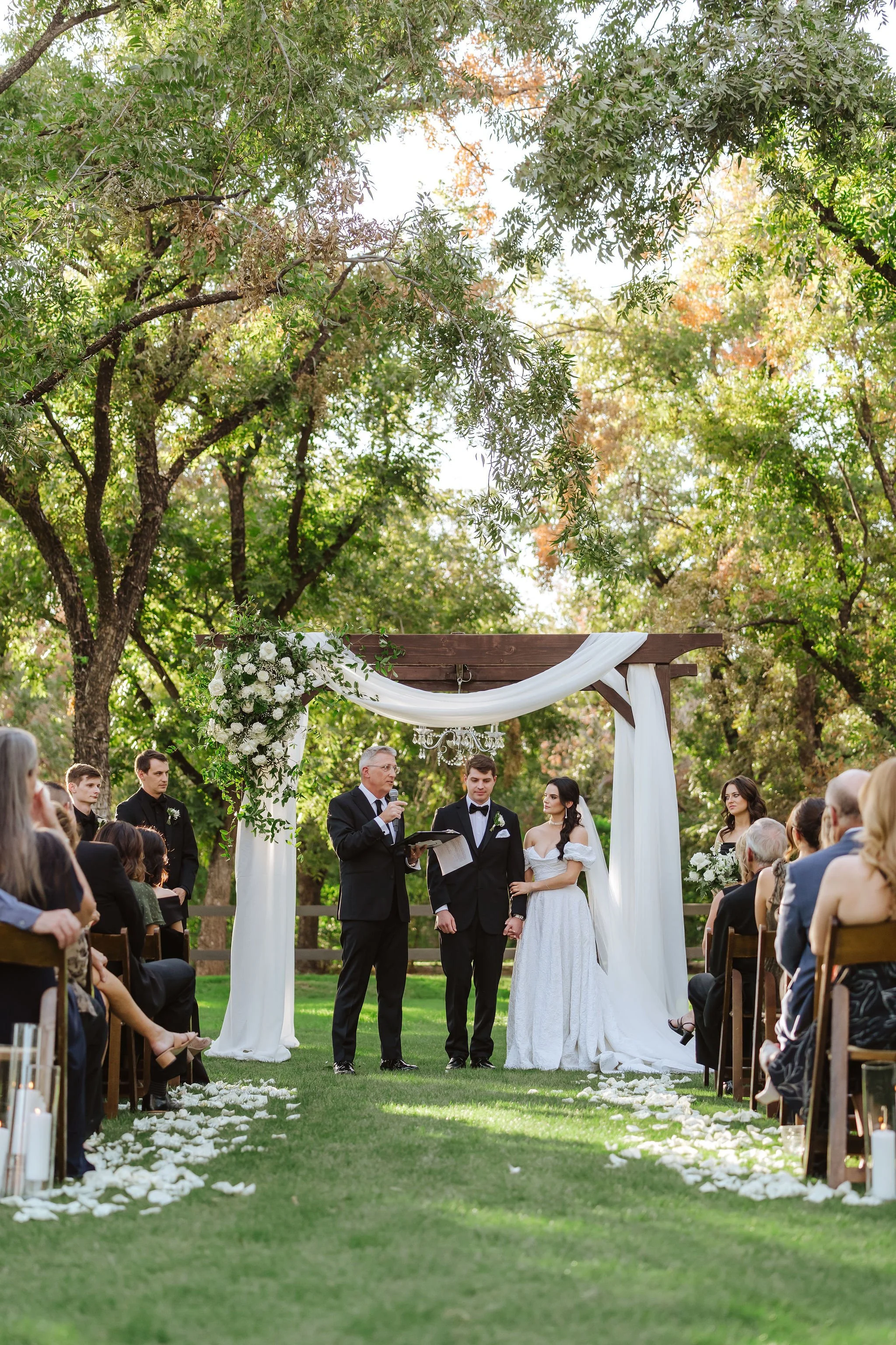 Bride and groom exchanging vows beneath a romantic white and green floral ceremony installation at Venue at the Grove.