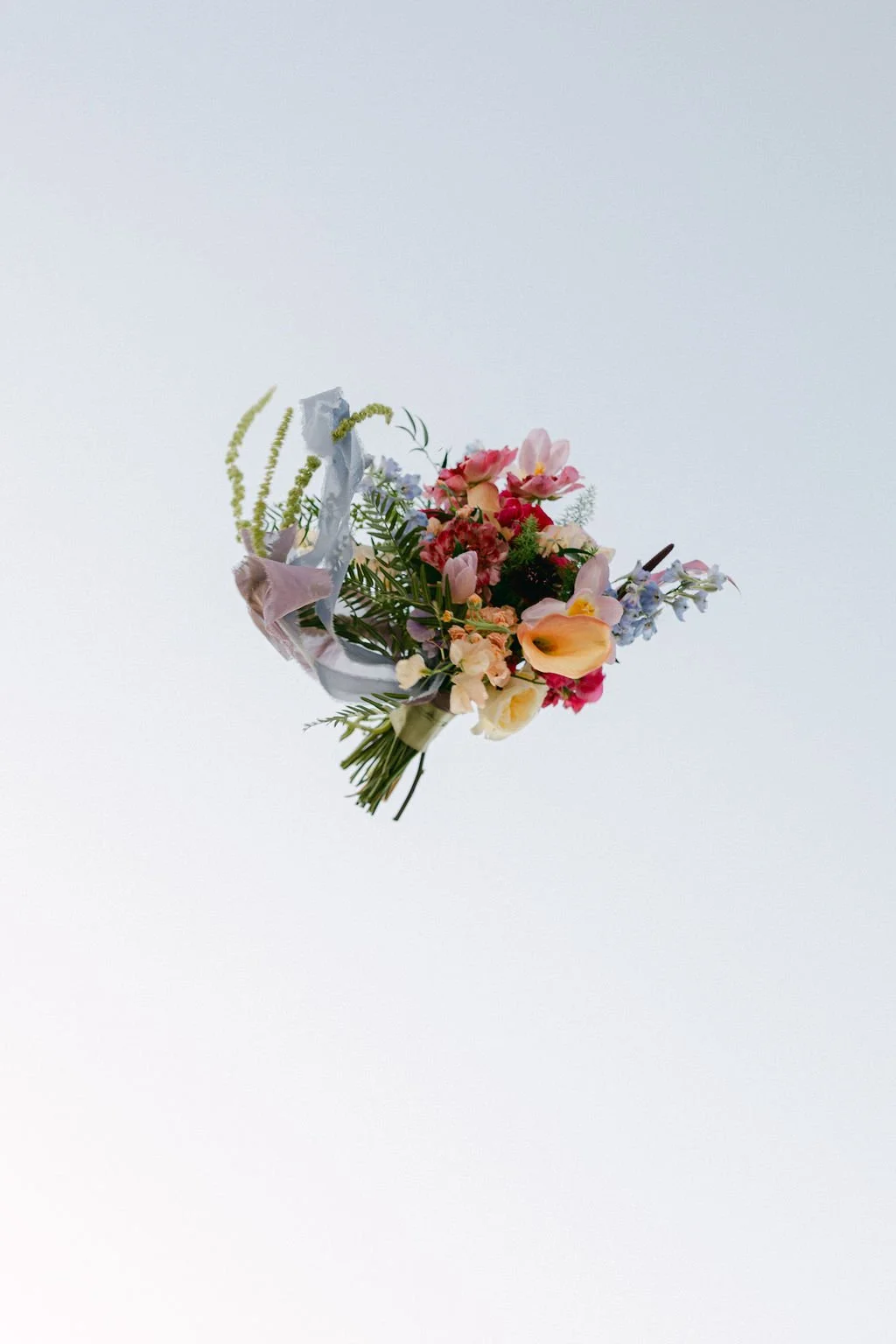 Artistic detail of a colorful garden-style bridal bouquet featuring bright pink, orange and purple flowers.
