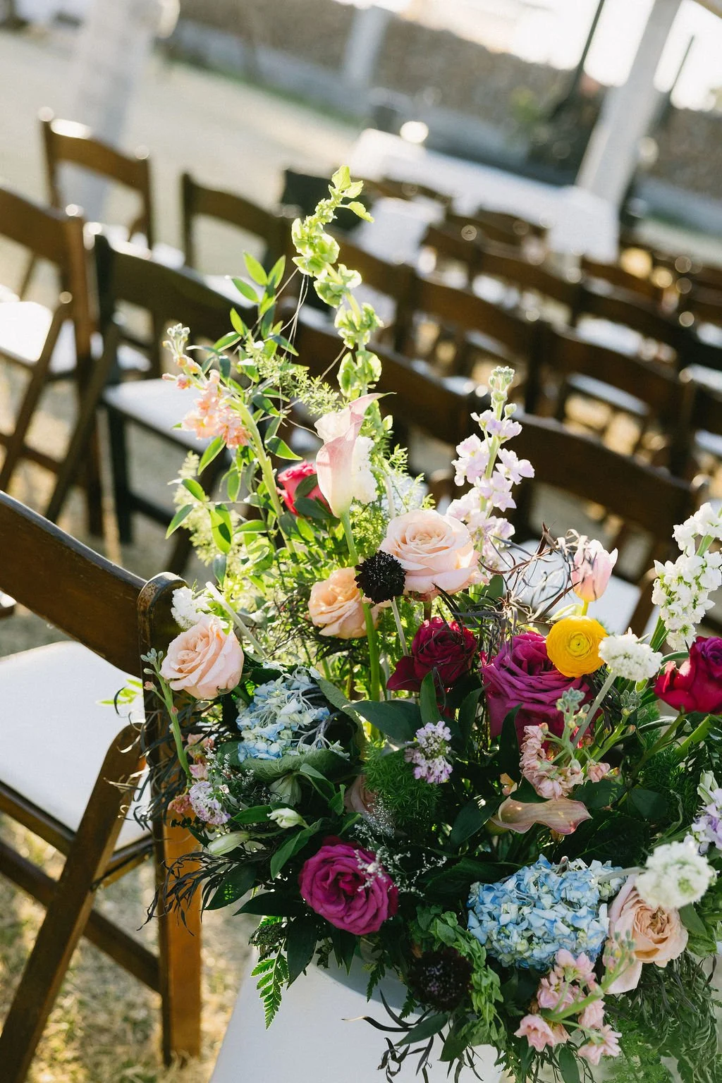 Vibrant garden-style wedding arrangement with pink, yellow, purple and orange flowers and organic greenery.