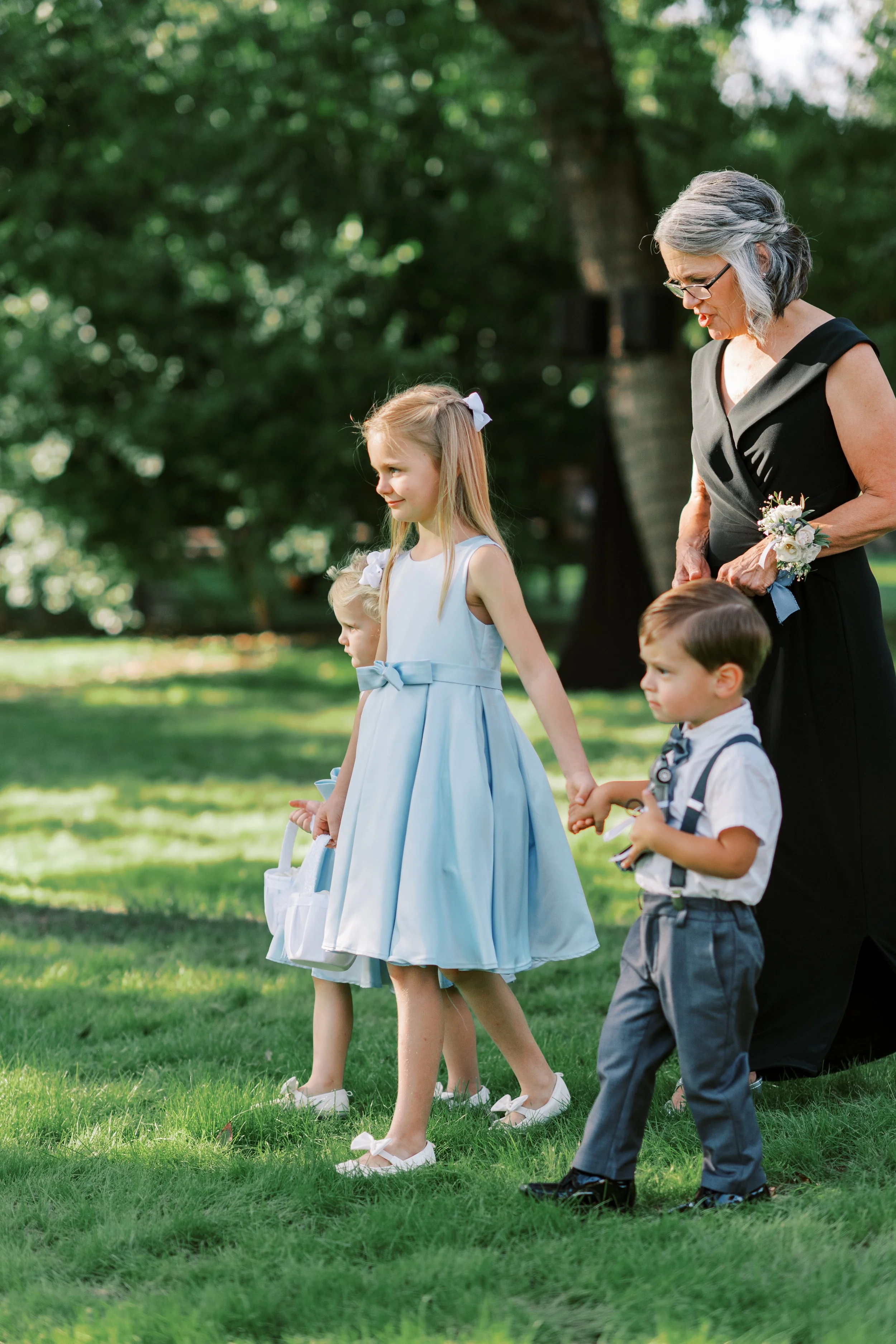 Flower girl in a light blue dress walking down the aisle at an outdoor garden wedding.