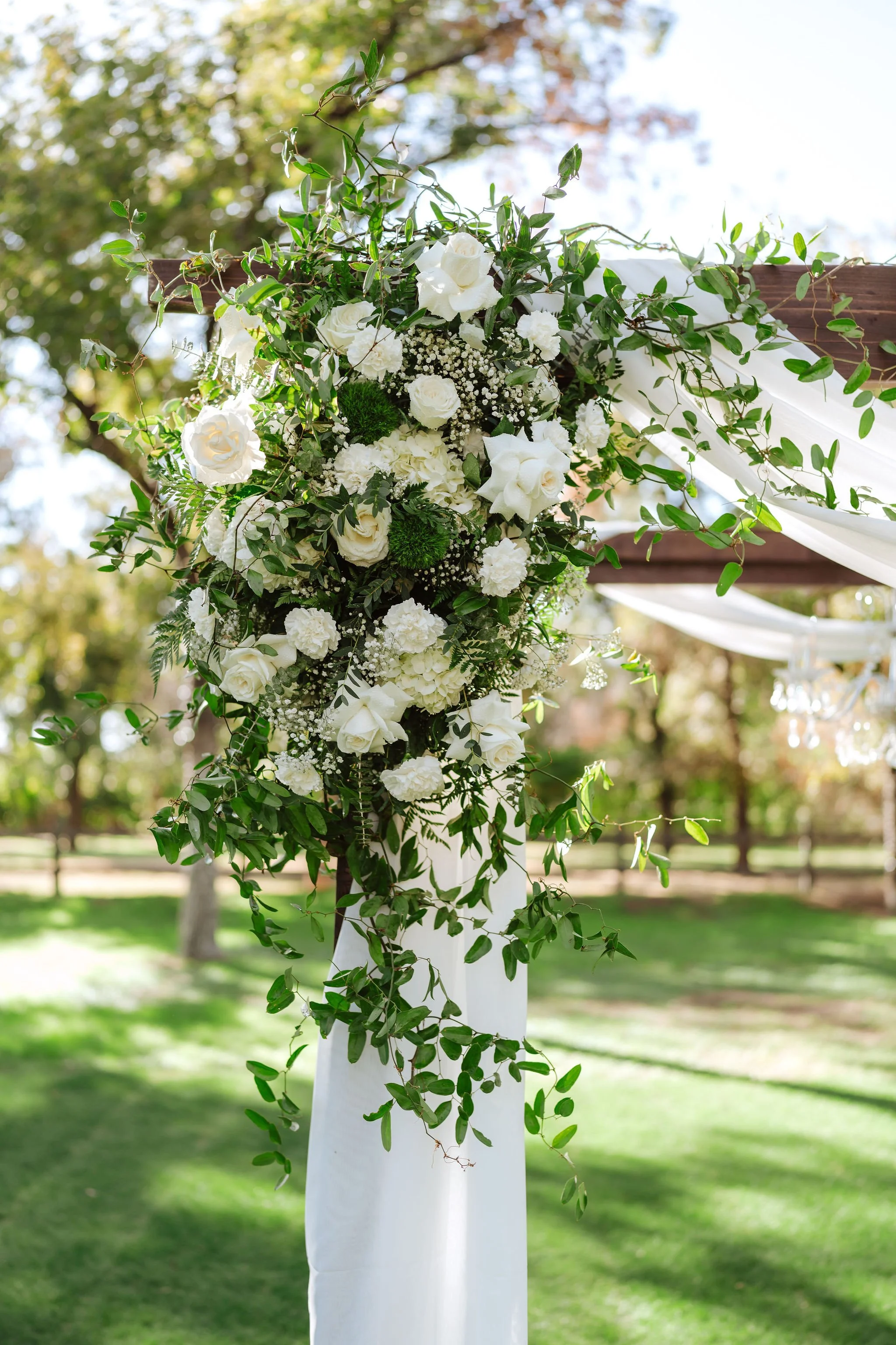 Lush white and green wedding ceremony floral installation with roses and cascading greenery at Venue at the Grove.