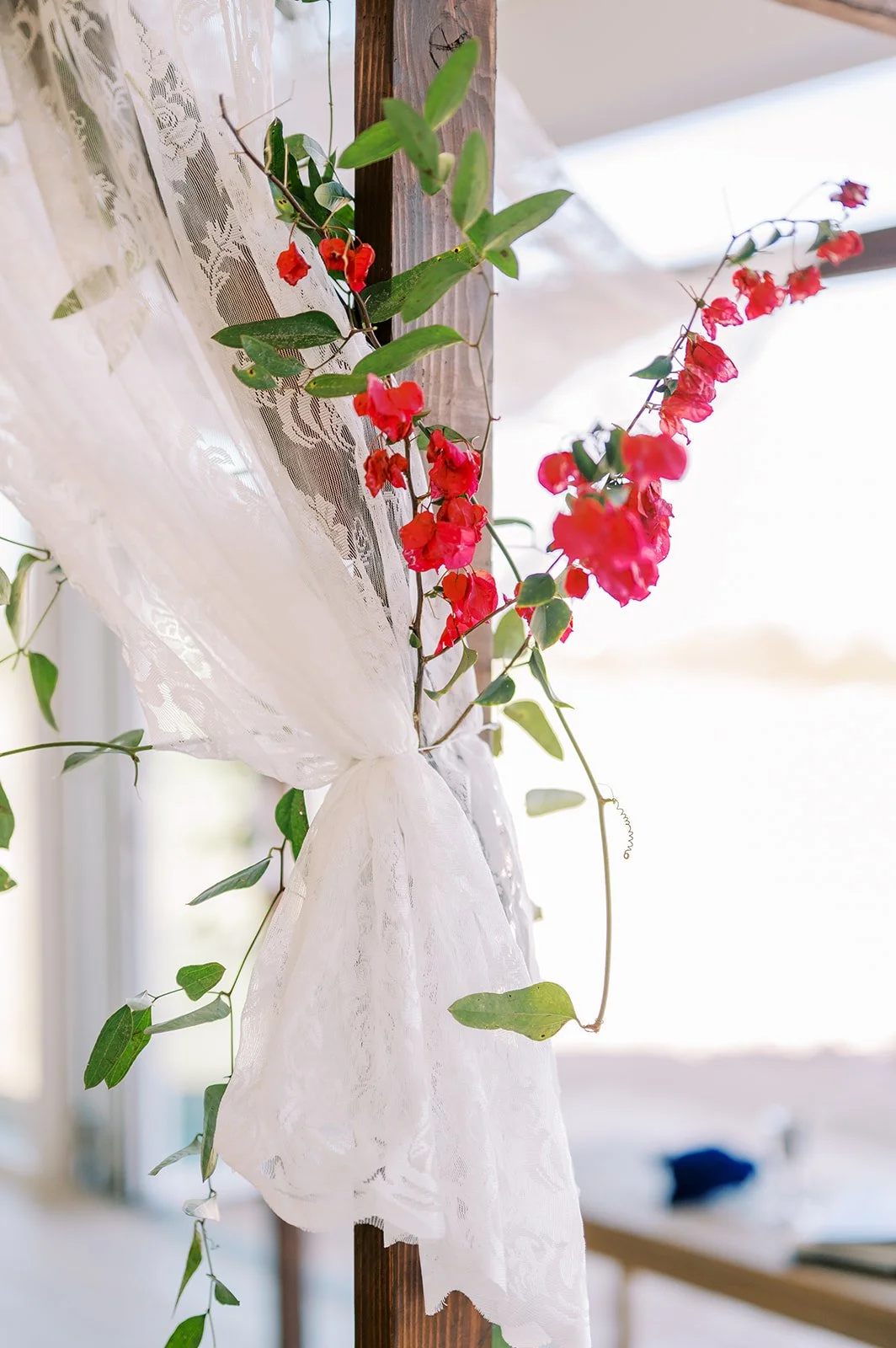 Close-up of vibrant red flowers and greenery cascading from a colorful wedding ceremony installation.