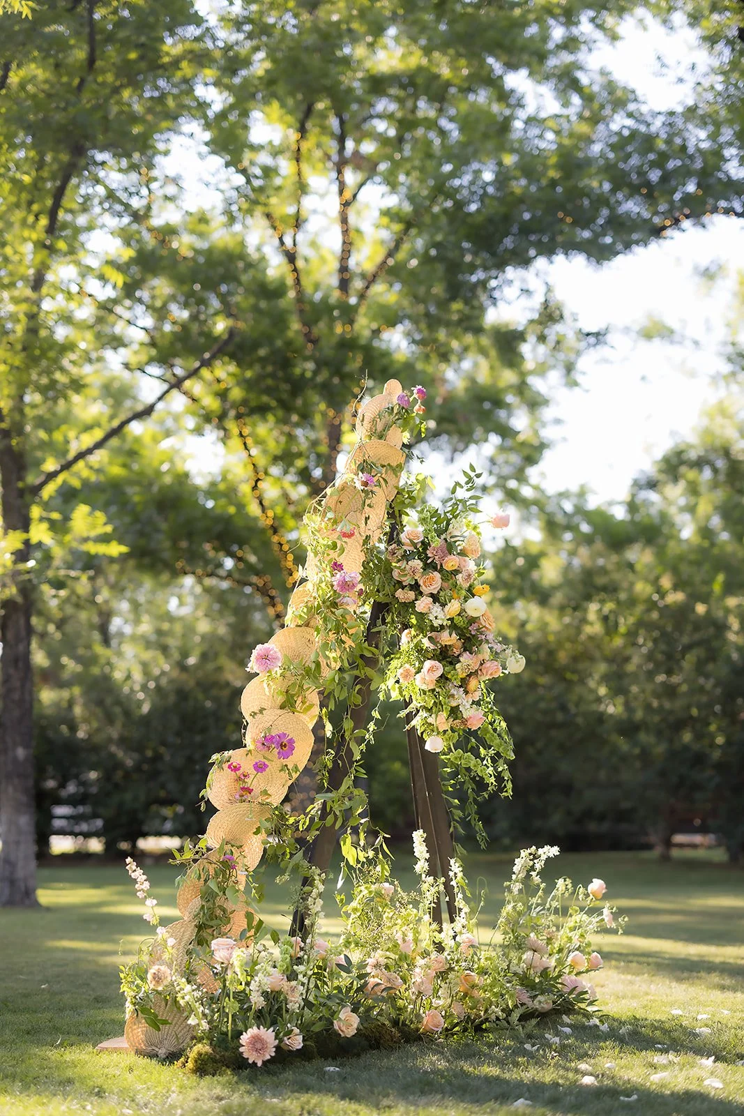 Organic wedding floral installation with peach, pink, yellow and lavender flowers beneath the trees at an Arizona outdoor ceremony.