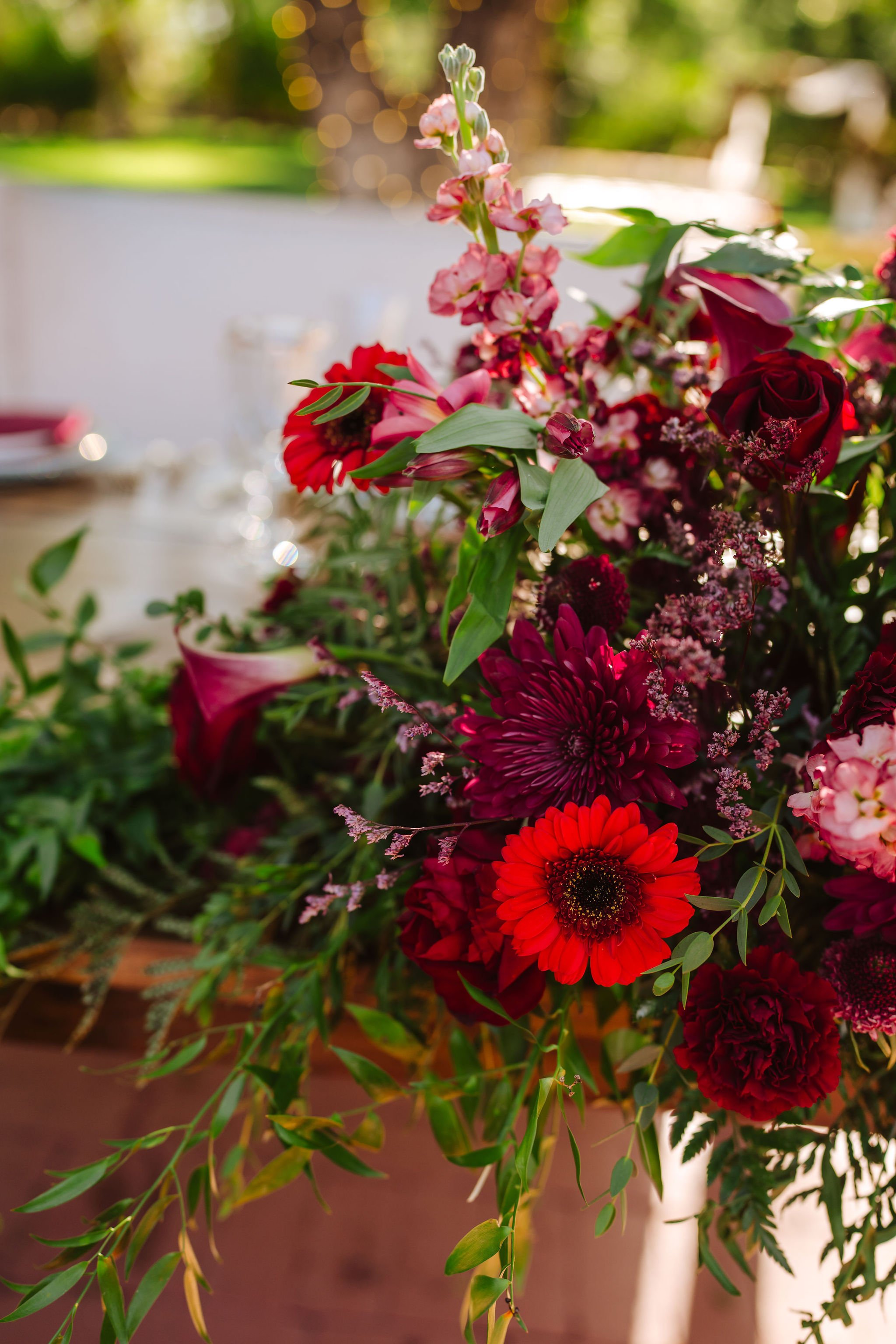 Dramatic red and burgundy wedding centerpiece featuring roses, lilies and vibrant garden-style flowers.