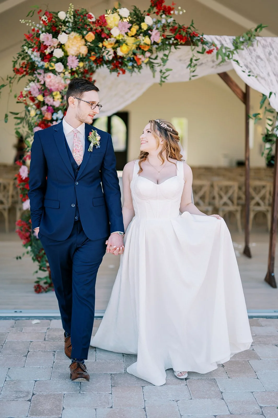 Newlyweds walking beneath a vibrant floral ceremony installation at their Desert View wedding.