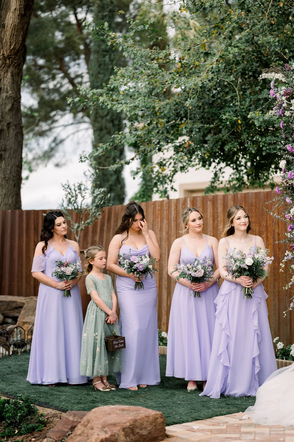 Bridesmaids in lavender dresses carrying coordinated garden-style bouquets with white, pink and purple flowers.