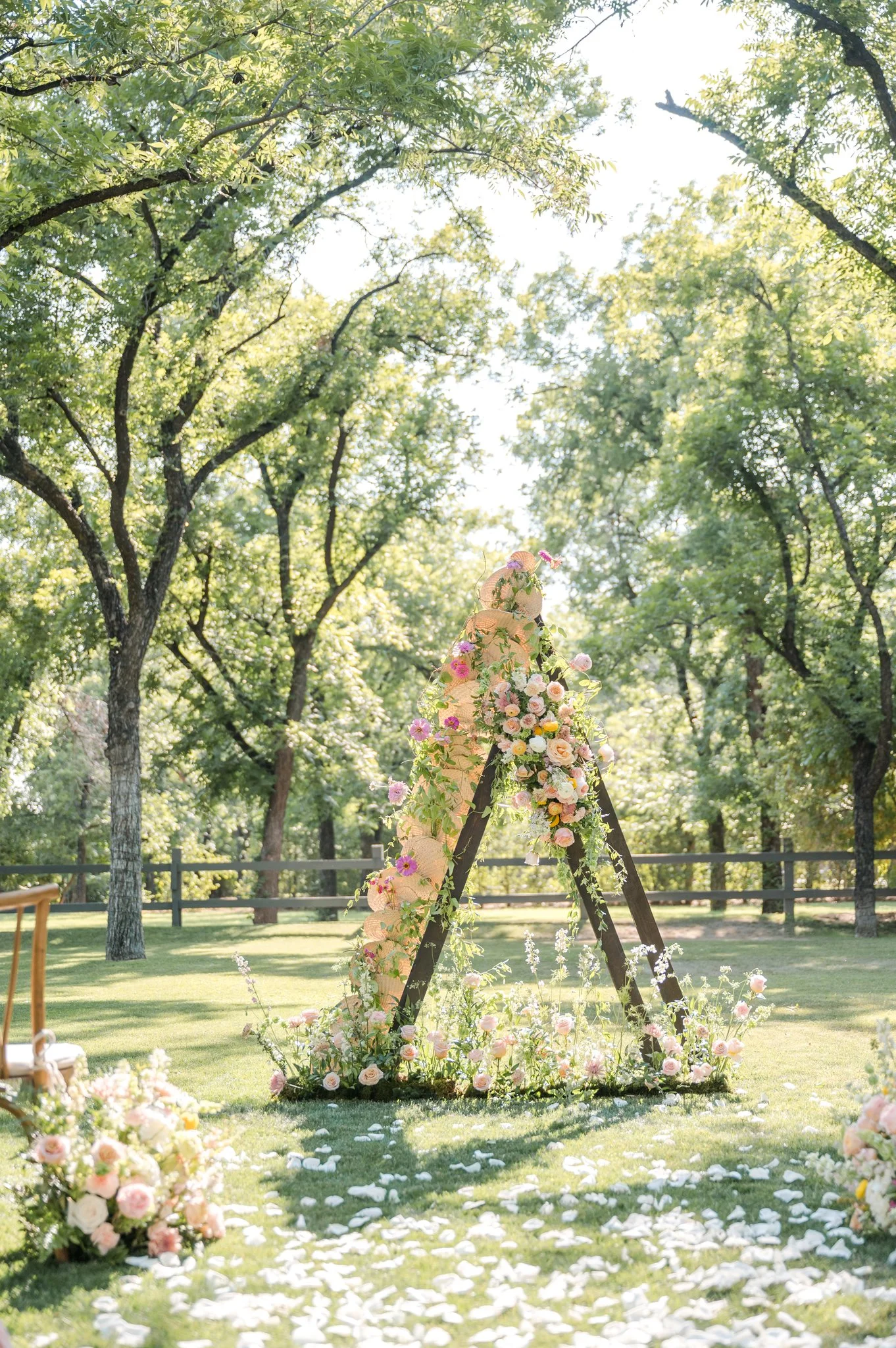 Outdoor wedding ceremony with a colorful triangular floral installation and flower-lined aisle.