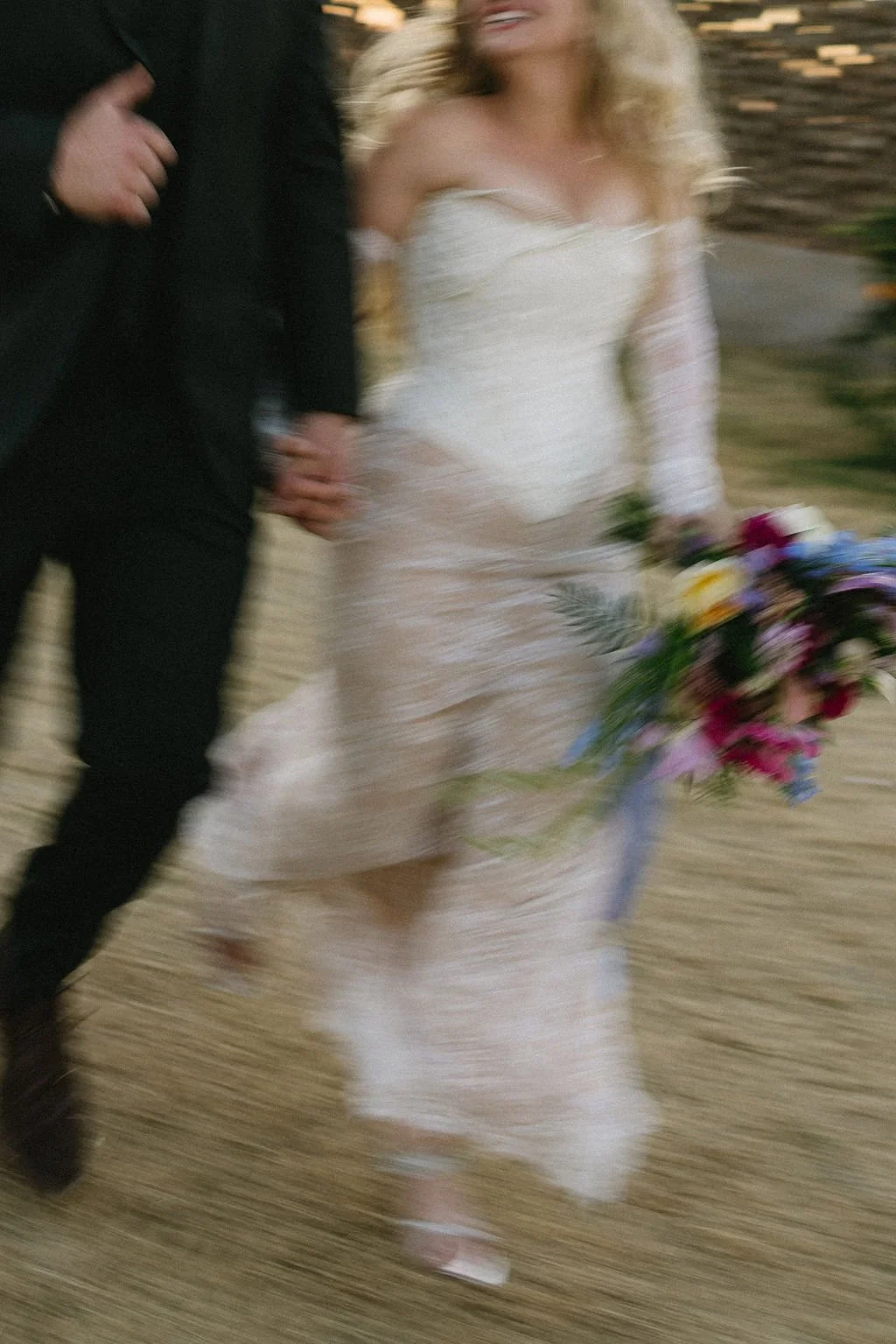 Bride walking with a vibrant cascading bouquet of pink and purple garden-style wedding flowers.
