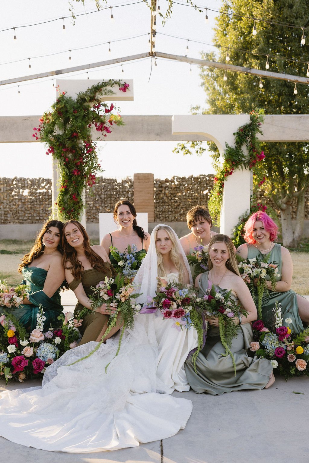Bride and wedding party celebrating beneath a colorful floral installation at an Arizona backyard wedding.